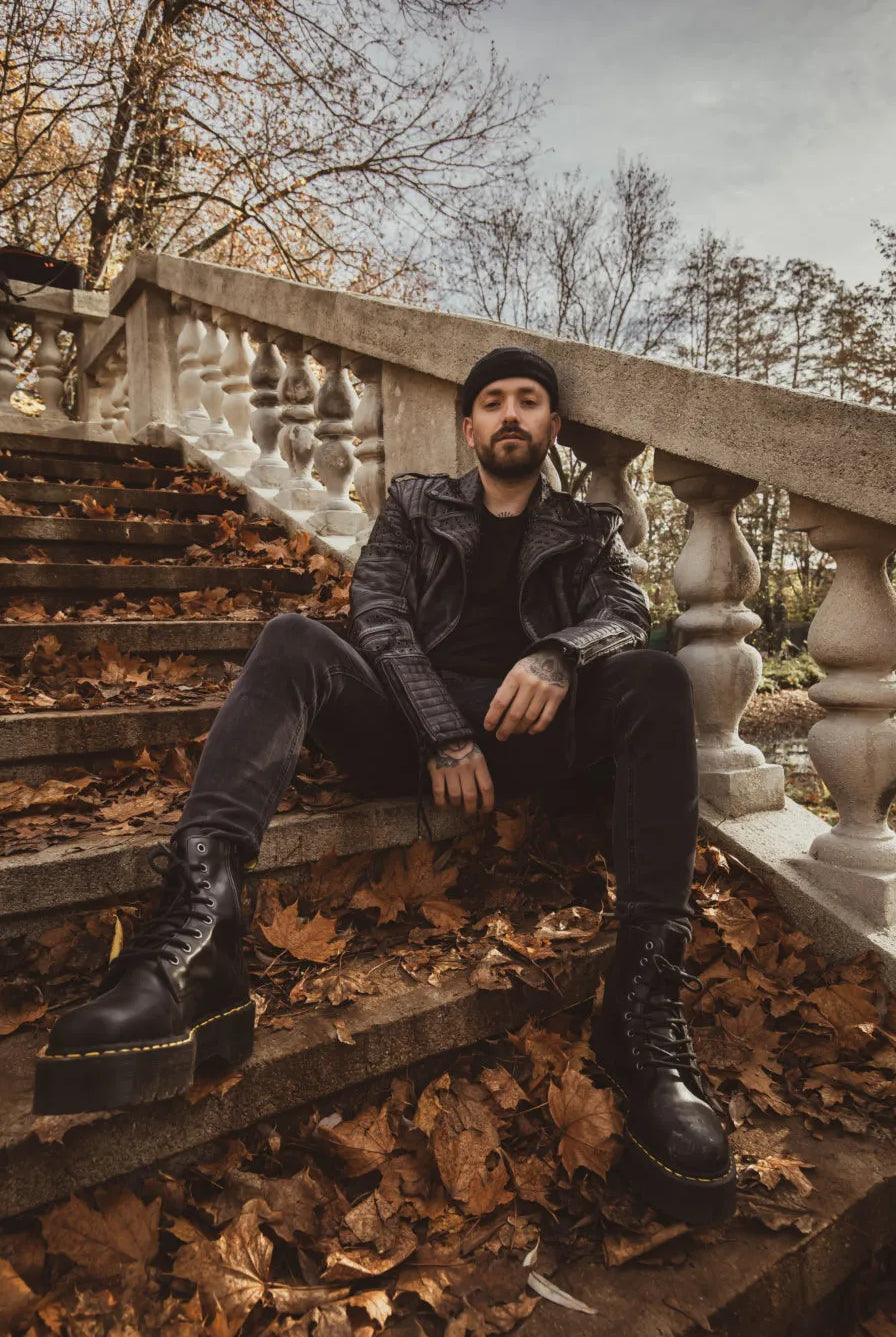 Model hat eine Lederjacke mit nieten an und eine Mütze sitzt auf einer Treppe in winterlicher Atmosphäre