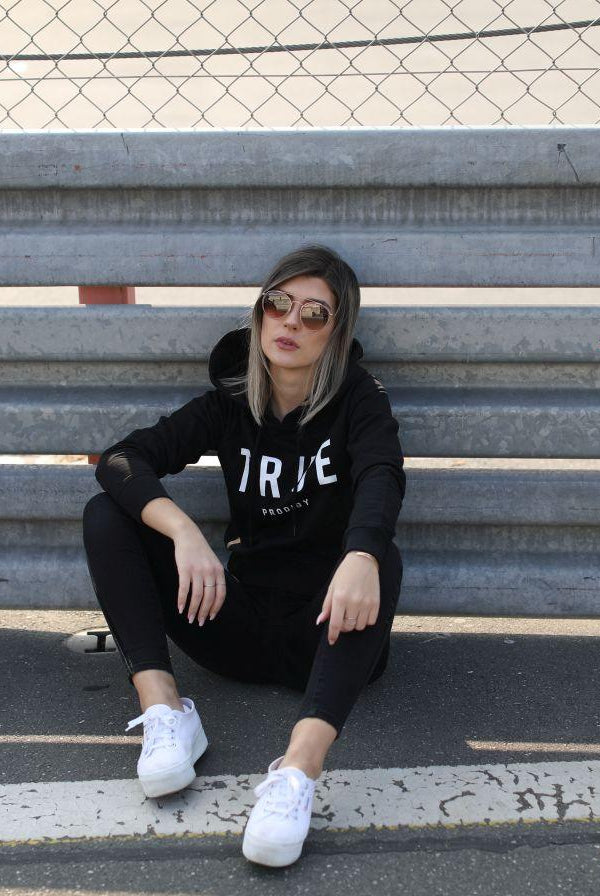 Damenmodel mit Sweater sitzend vor Leitplanke auf Rennbahn