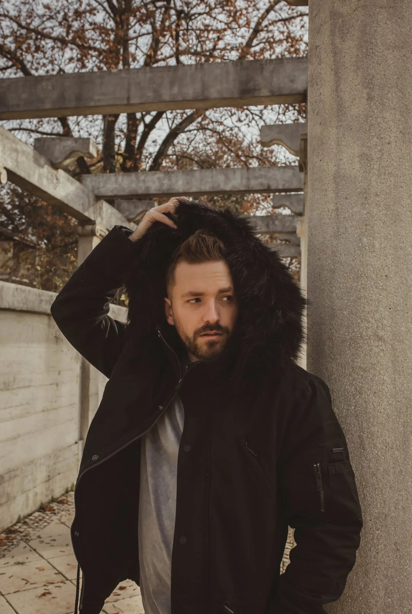 Herrenmodel mit Winterjacke und Kapuze in schwarz vor herbstlichem Hintergrund