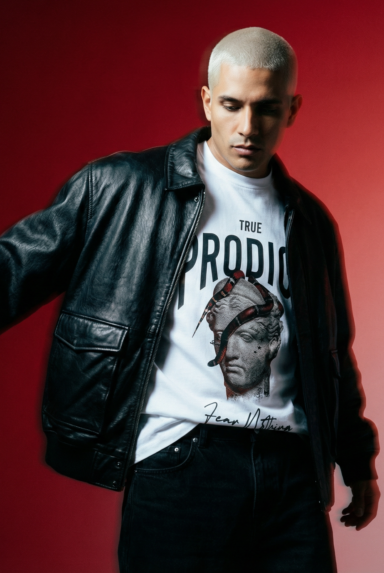 Ein Mann in schwarzer Lederjacke und Sonnenbrille steht im Freien und blickt in die Kamera. Der Hintergrund wirkt sonnig und unscharf, man sieht Grünflächen und Gebäude.