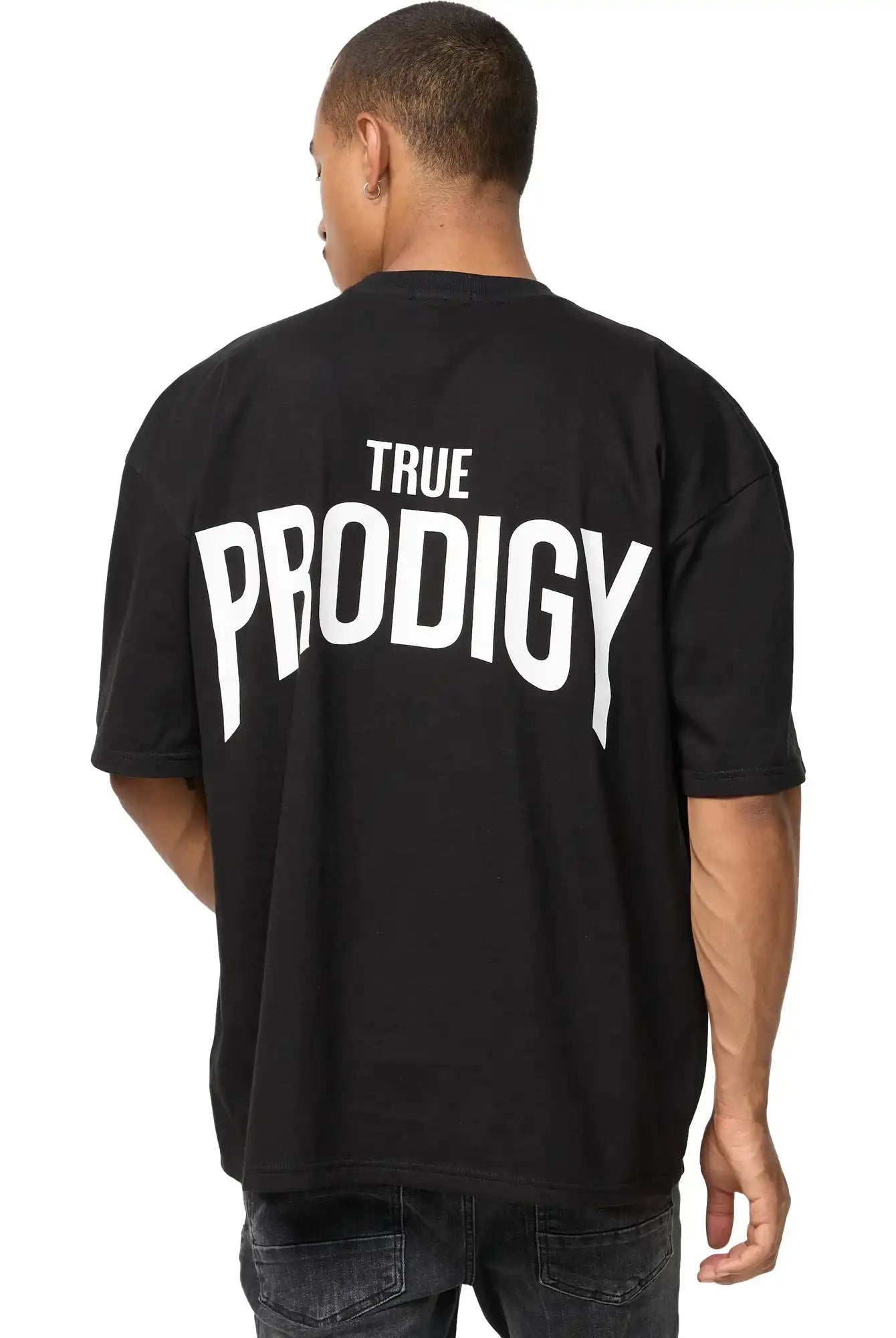 Eine Person blickt von der Kamera weg und trägt das trueprodigy Jona Oversized T-Shirt mit Druck in schwarz mit dem Aufdruck TRUE PRODIGY in fetten weißen Buchstaben auf dem Rücken, gepaart mit einer dunklen Jeans.