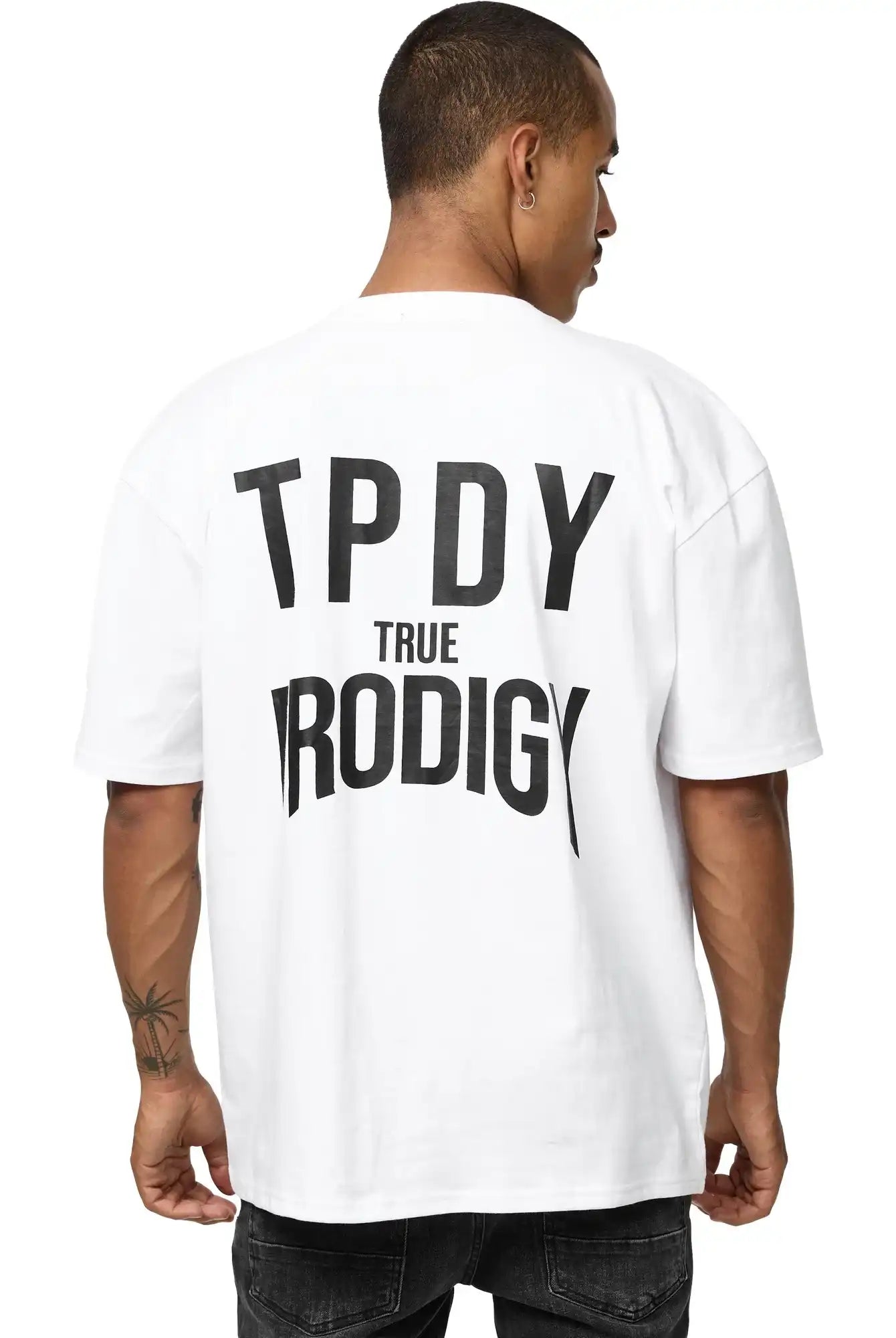 Ein Mann mit kurzen Haaren blickt von der Kamera weg, er trägt das Robin Oversized T-Shirt mit Druck von trueprodigy; "TPDY TRUE PRODIGY" steht fett in schwarz auf der Rückseite seines Unisex-Shirts aus schwerem Jersey.