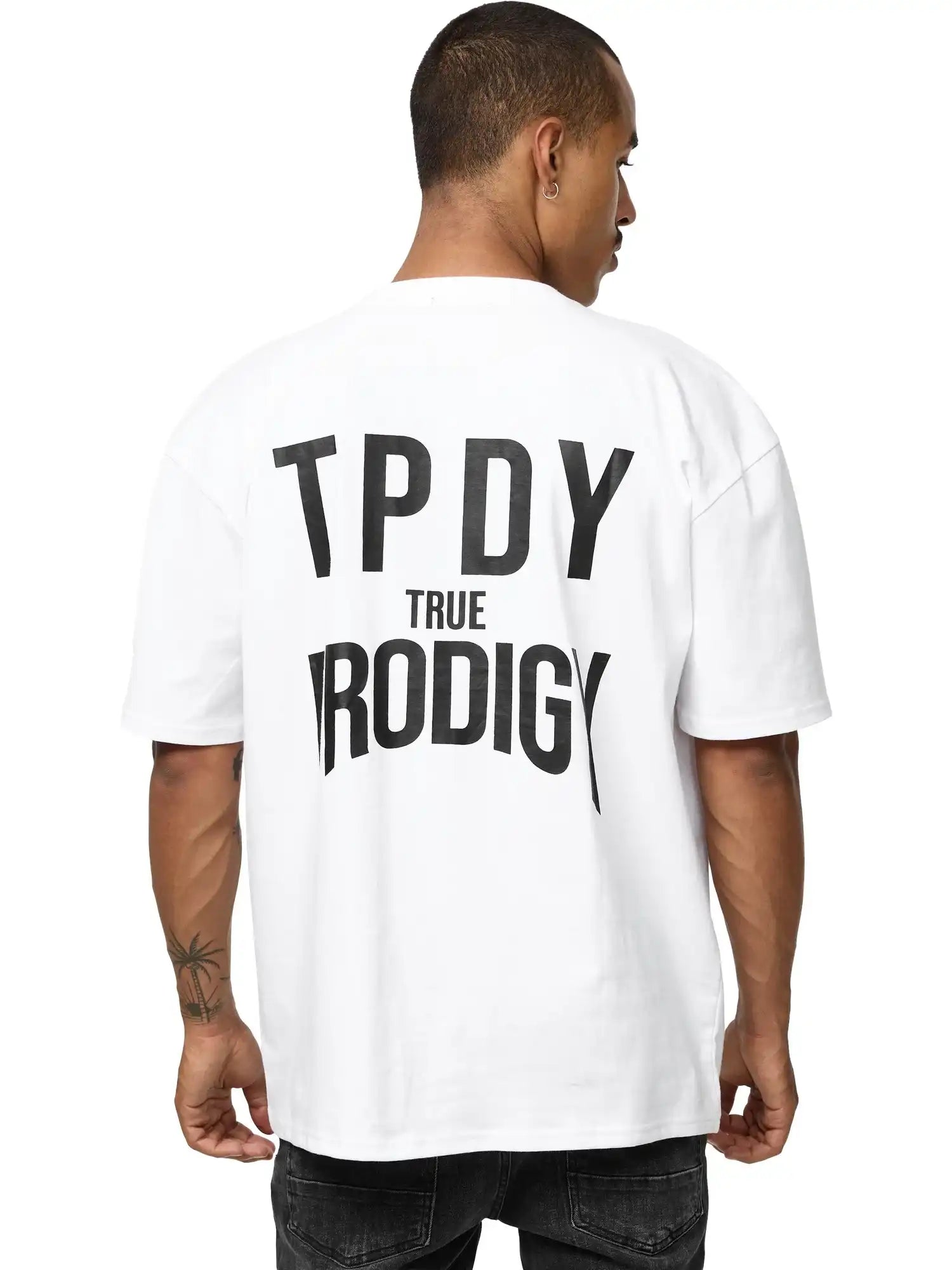 Ein Mann mit kurzen Haaren blickt von der Kamera weg, er trägt das Robin Oversized T-Shirt mit Druck von trueprodigy; "TPDY TRUE PRODIGY" steht fett in schwarz auf der Rückseite seines Unisex-Shirts aus schwerem Jersey.