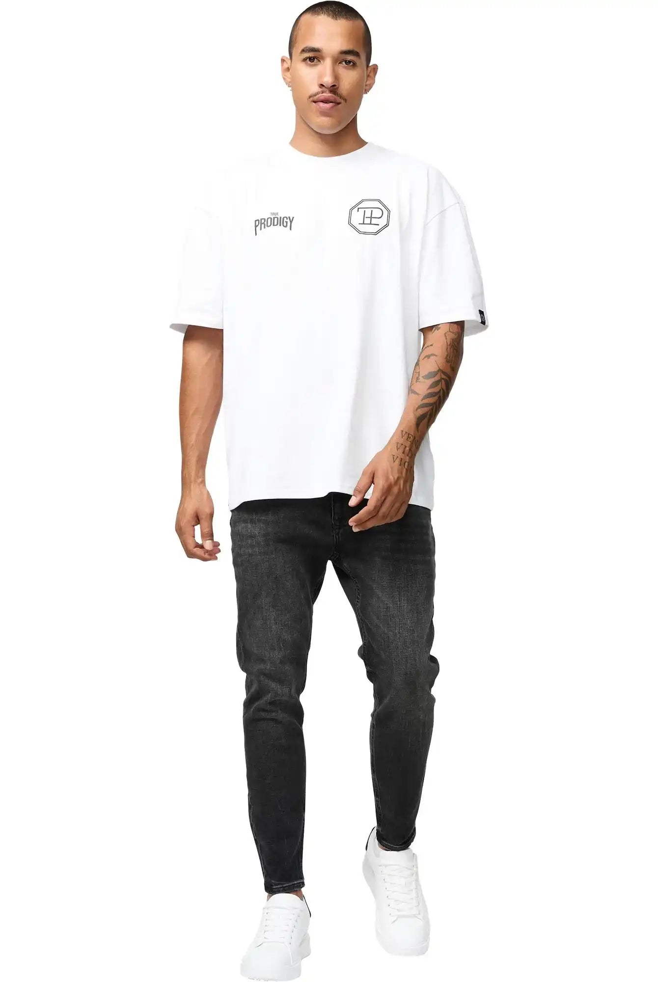 Ein Mann mit kurzen Haaren und einem Schnurrbart trägt das Robin Oversized T-Shirt mit Druck von trueprodigy, gepaart mit schwarzen Jeans und weißen Turnschuhen, während er vor einem schlichten weißen Hintergrund nach vorne geht.