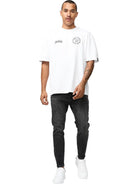 Ein Mann mit kurzen Haaren und einem Schnurrbart trägt das Robin Oversized T-Shirt mit Druck von trueprodigy, gepaart mit schwarzen Jeans und weißen Turnschuhen, während er vor einem schlichten weißen Hintergrund nach vorne geht.