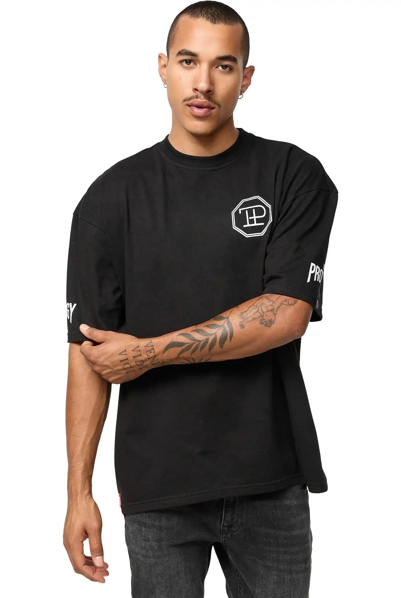 Eine Person mit kurzen Haaren und Schnurrbart trägt das trueprodigy Dilan Oversized T-Shirt mit Druck-schwarz, unisex, mit weißen grafischen Prints auf Brust und Ärmeln-gepaart mit dunklen Jeans, vor einem schlichten weißen Hintergrund.