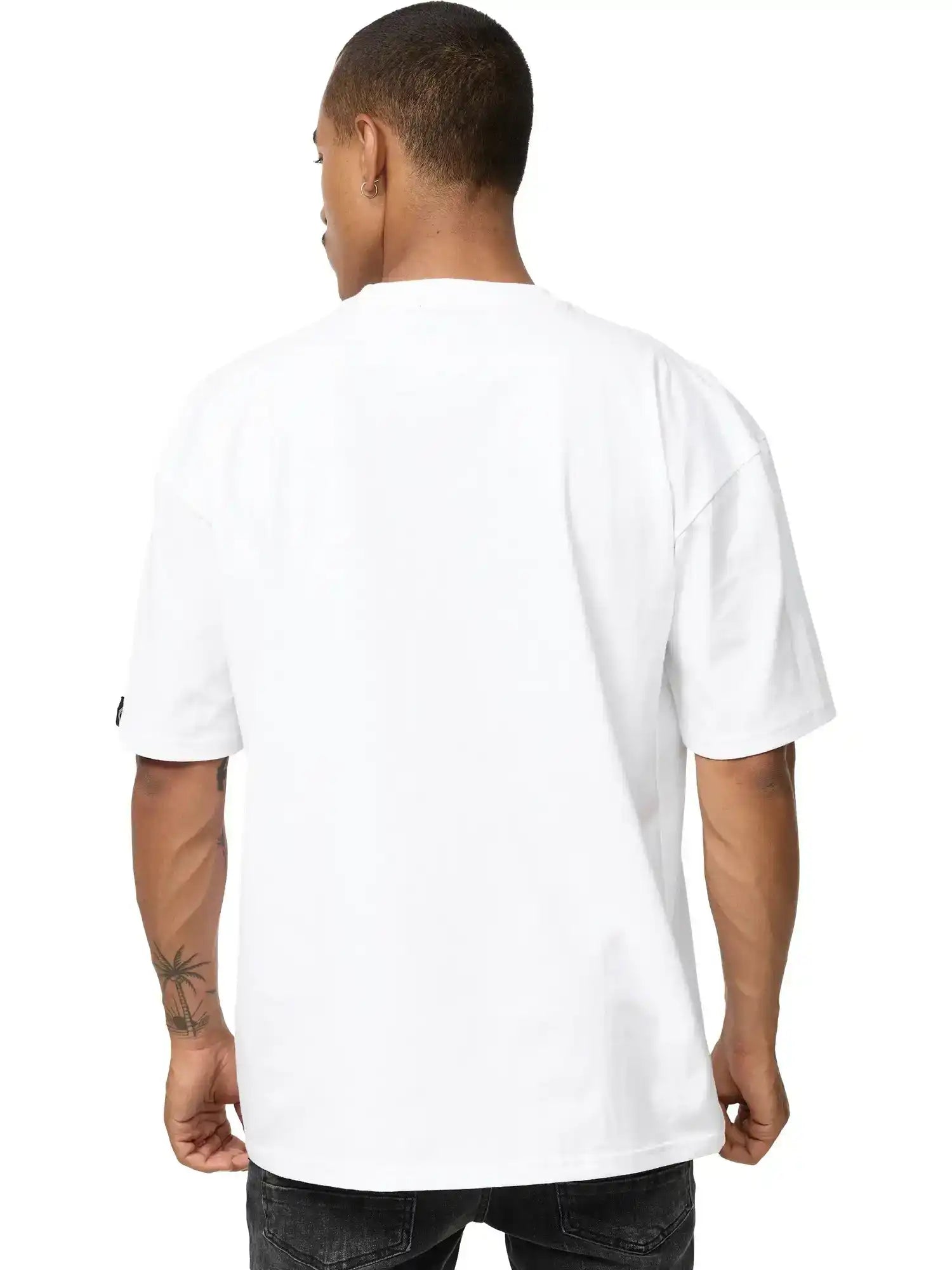 Eine Person mit kurzen Haaren und einer Tätowierung am linken Unterarm blickt von der Kamera weg und trägt ein schlichtes weißes trueprodigy Phoenix Oversized T-Shirt mit Stehkragen und dunkle Jeans.