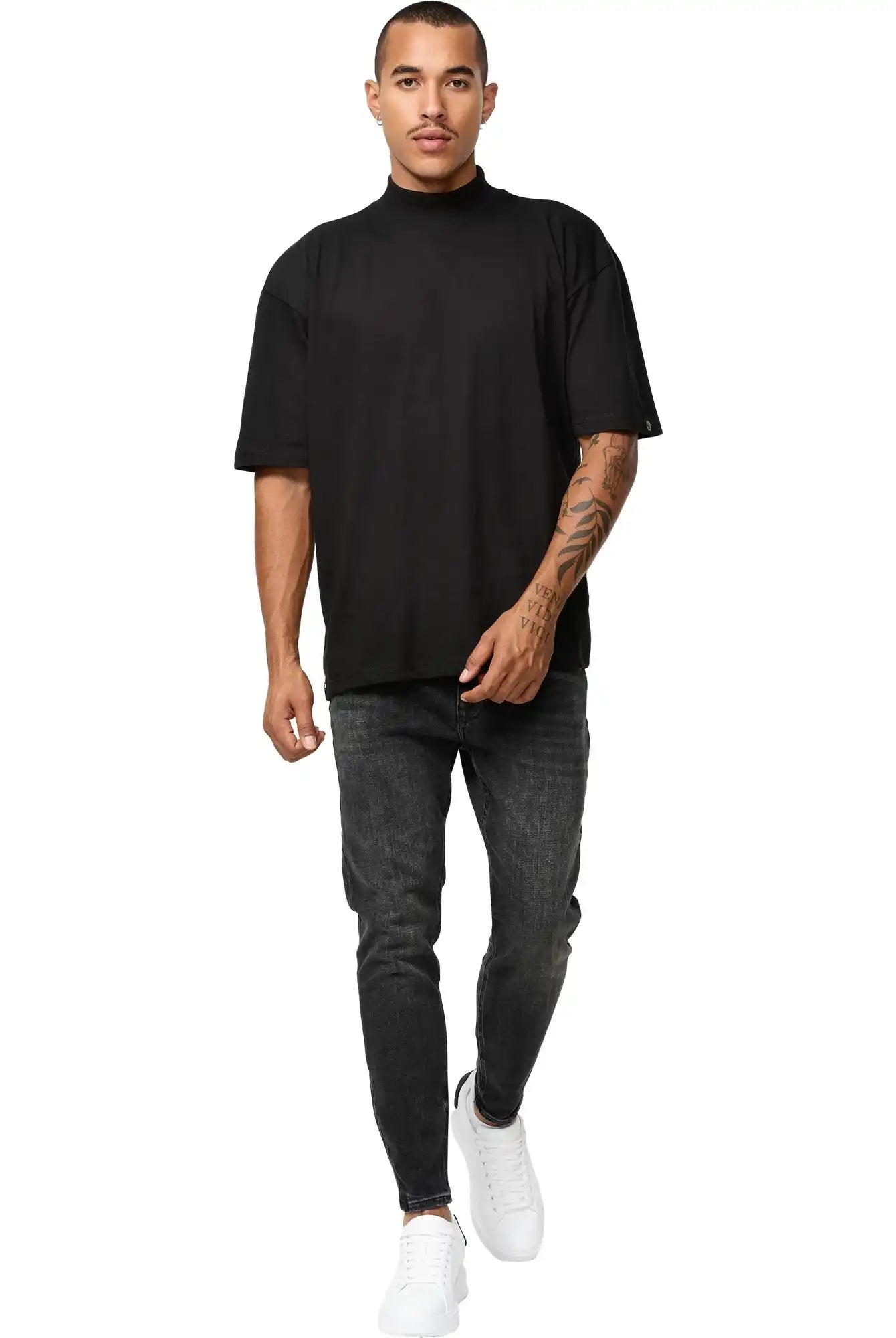 Ein Mann mit kurzen Haaren und einem sichtbaren Tattoo auf dem rechten Arm geht mit neutraler Miene nach vorne. Er trägt das trueprodigy Phoenix Oversized T-Shirt mit Stehkragen, dunkelgraue Jeans und weiße Turnschuhe vor einem schlichten weißen Hintergrund.