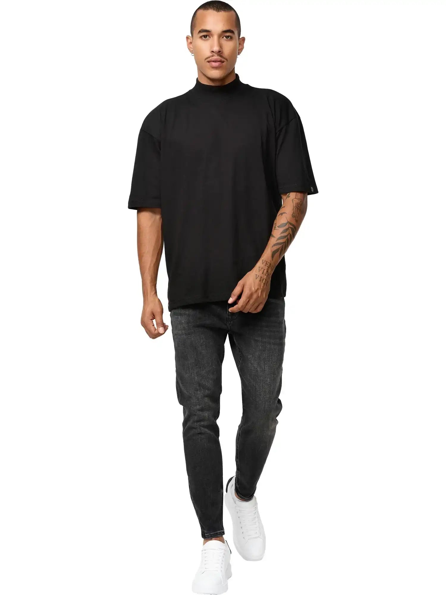 Ein Mann mit kurzen Haaren und einem sichtbaren Tattoo auf dem rechten Arm geht mit neutraler Miene nach vorne. Er trägt das trueprodigy Phoenix Oversized T-Shirt mit Stehkragen, dunkelgraue Jeans und weiße Turnschuhe vor einem schlichten weißen Hintergrund.