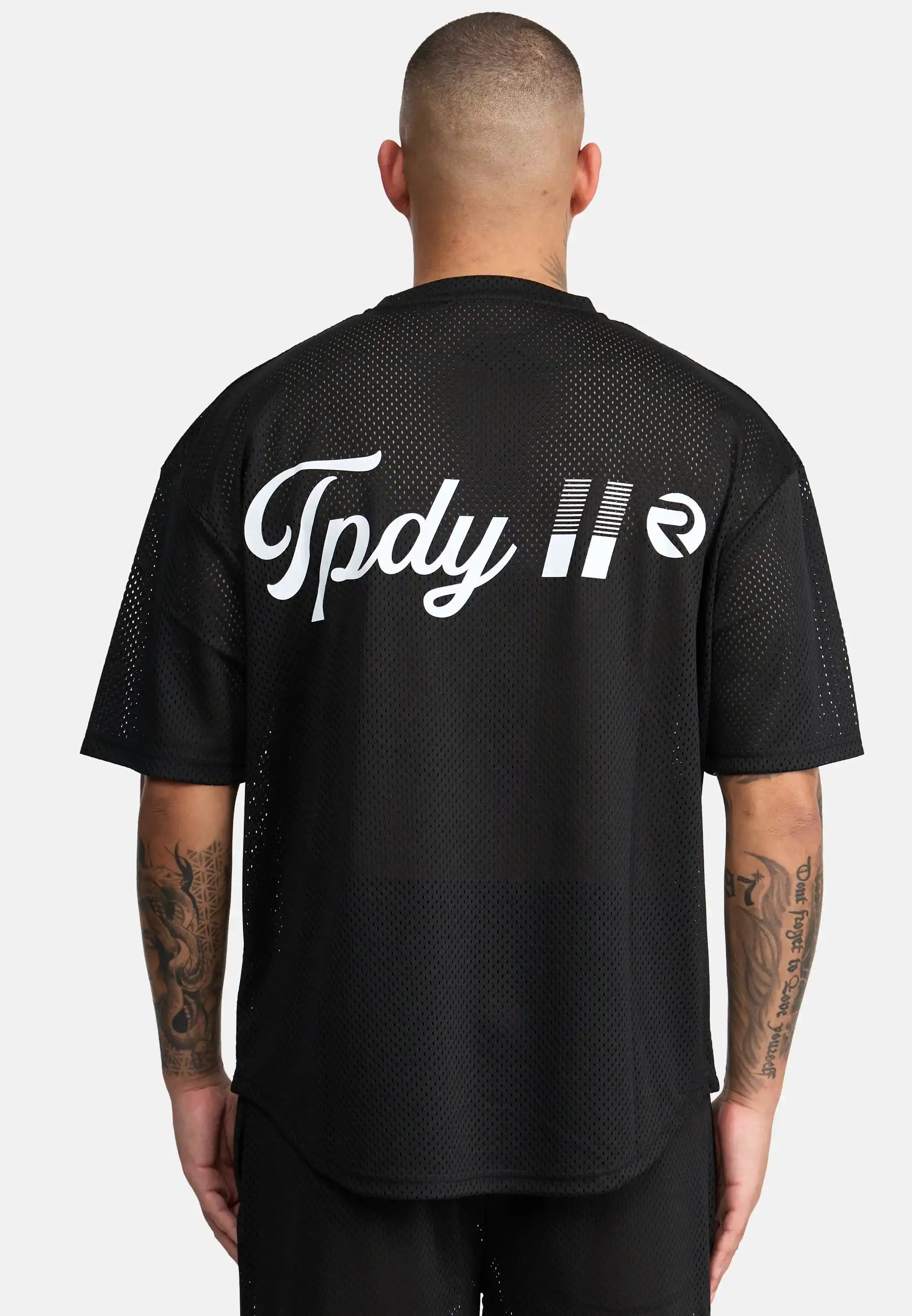 Eine Person mit kurzen Haaren und tätowierten Armen blickt in die Ferne. Sie trägt das trueprodigy Daniel Oversized T-Shirt mit Druck in schwarzem Mesh mit dem Schriftzug "Tpdy II" und einem kreisförmigen weißen Logo auf dem Rücken vor einem schlichten weißen Hintergrund.