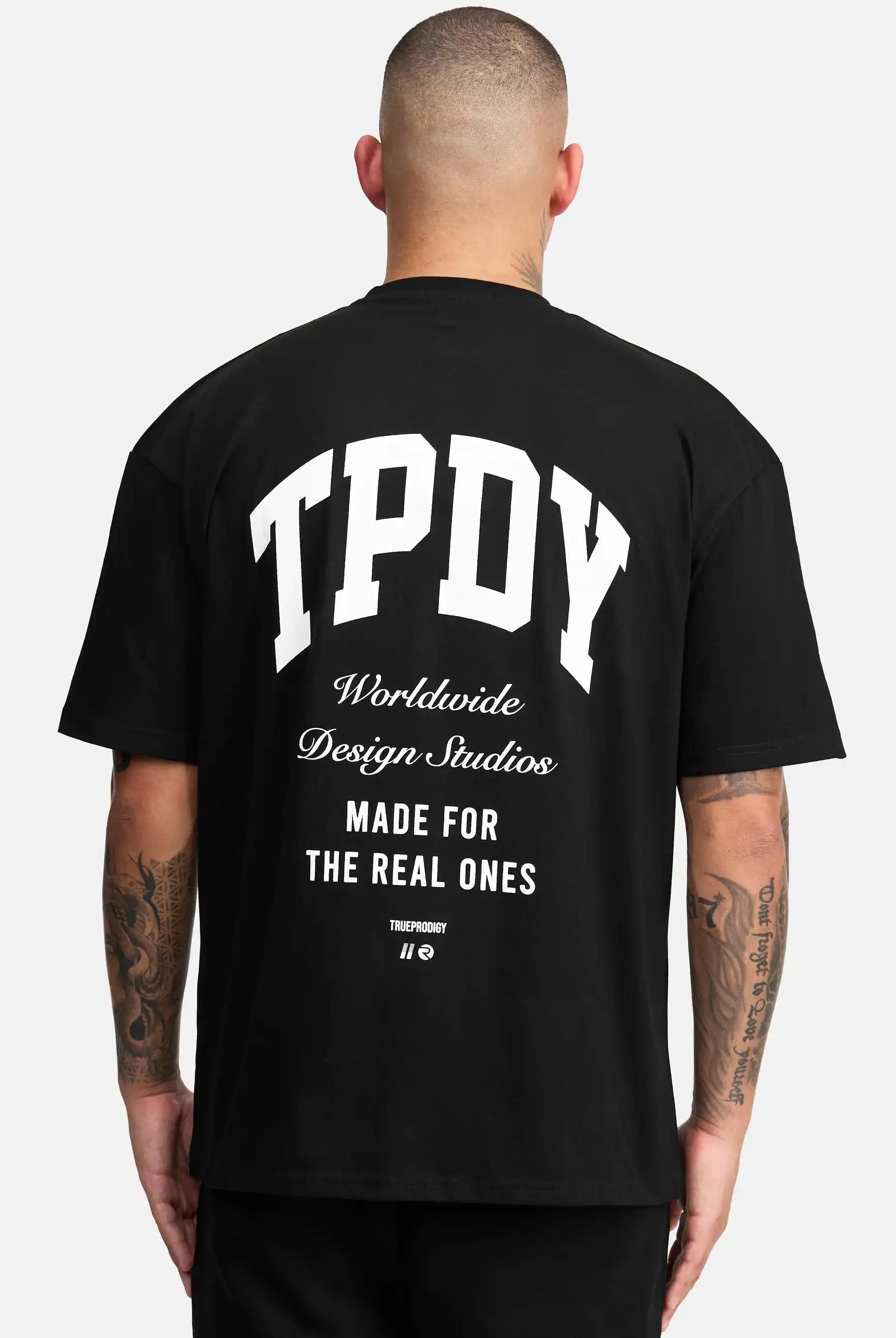 Das Elijah Oversized T-Shirt mit Druck von trueprodigy mit dem Schriftzug "TPDY Worldwide Design Studios Made for the real ones" in Weiß auf dem Rücken, der den schweren Jersey-Stoff hervorhebt, zeigt eine Person mit kurzen Haaren.