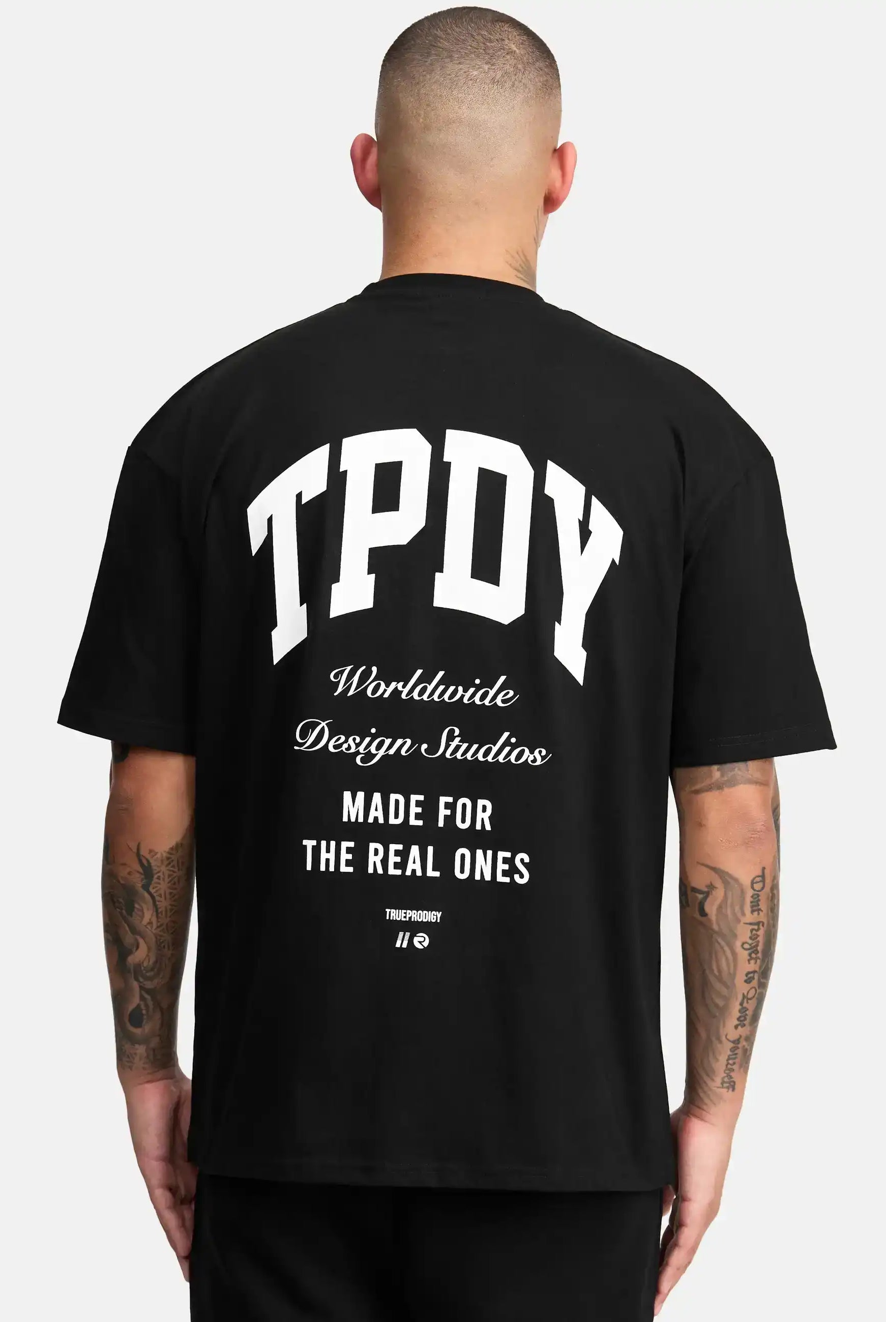 Das Elijah Oversized T-Shirt mit Druck von trueprodigy mit dem Schriftzug "TPDY Worldwide Design Studios Made for the real ones" in Weiß auf dem Rücken, der den schweren Jersey-Stoff hervorhebt, zeigt eine Person mit kurzen Haaren.