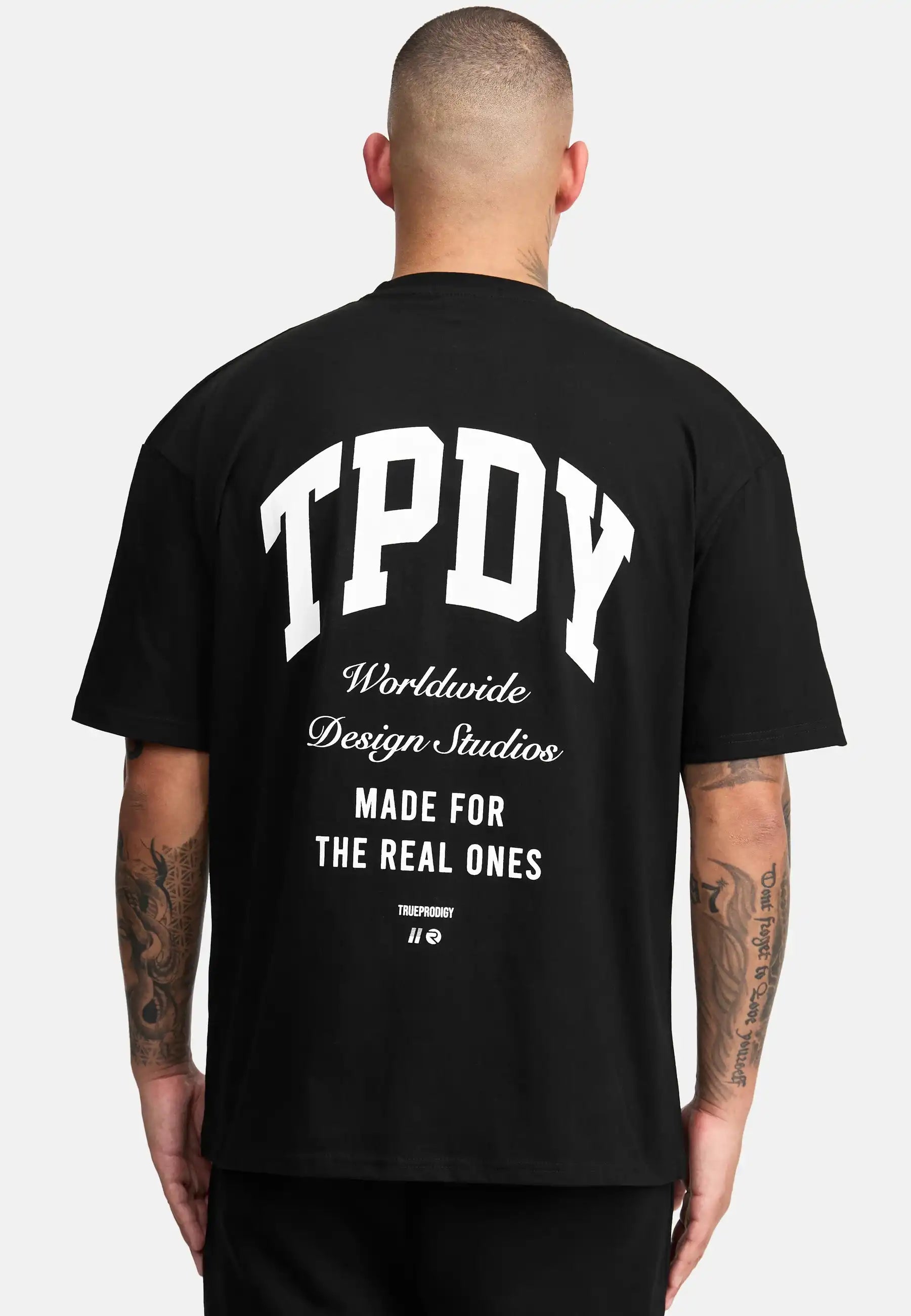 Das Elijah Oversized T-Shirt mit Druck von trueprodigy mit dem Schriftzug "TPDY Worldwide Design Studios Made for the real ones" in Weiß auf dem Rücken, der den schweren Jersey-Stoff hervorhebt, zeigt eine Person mit kurzen Haaren.