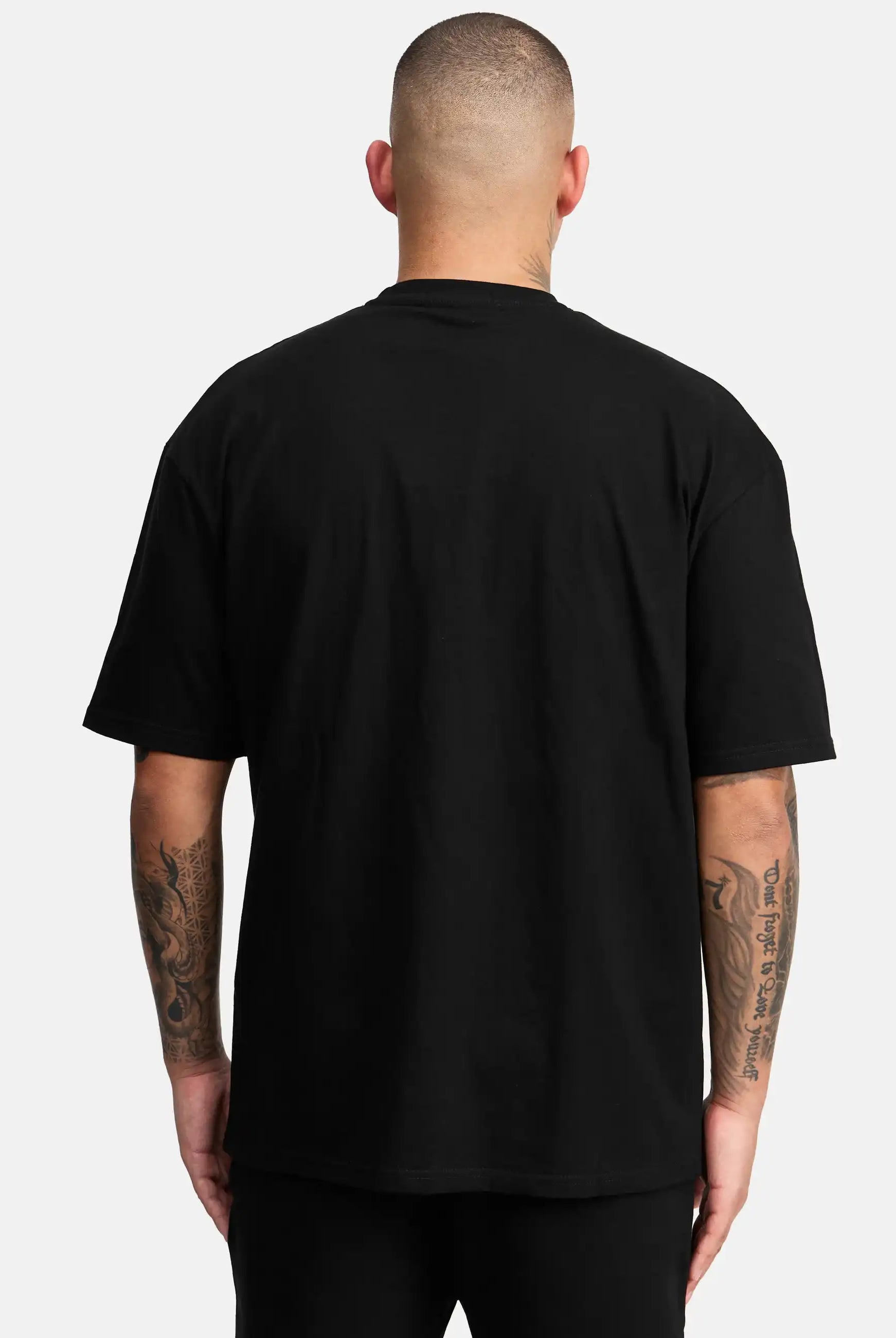 Eine Person mit kurzen Haaren und tätowierten Armen ist von hinten zu sehen. Sie trägt das trueprodigy Miguel Oversized T-Shirt mit Druck und eine schwarze Hose vor einem hellgrauen Hintergrund.