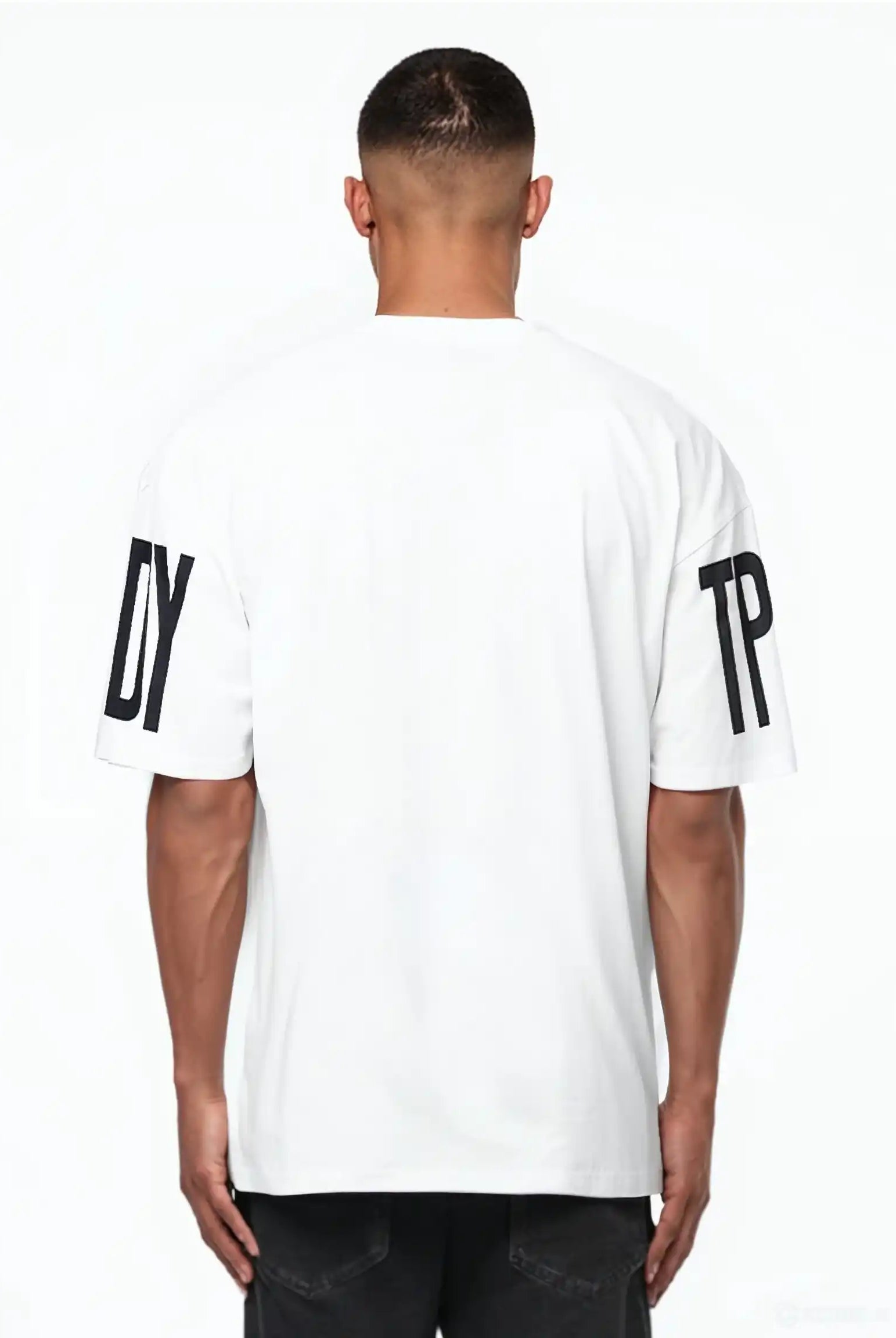 Ein Mann blickt von der Kamera weg und trägt das Viktor Oversize-Herren-T-Shirt von trueprodigy. Das weiße Unisex-Shirt hat schwarze DY- und TP-Prints auf den Ärmeln, die sich von einem unifarbenen Hintergrund aus schwerem Jersey-Stoff abheben.