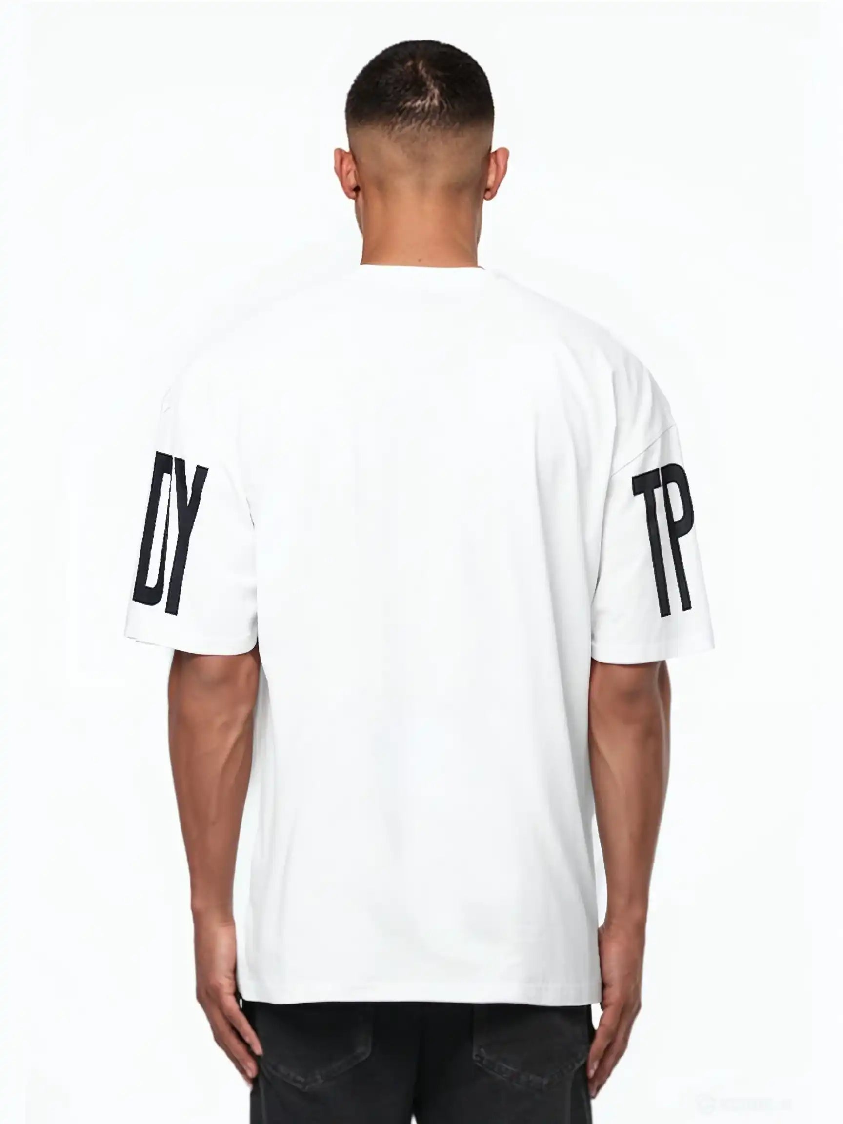 Ein Mann blickt von der Kamera weg und trägt das Viktor Oversize-Herren-T-Shirt von trueprodigy. Das weiße Unisex-Shirt hat schwarze DY- und TP-Prints auf den Ärmeln, die sich von einem unifarbenen Hintergrund aus schwerem Jersey-Stoff abheben.