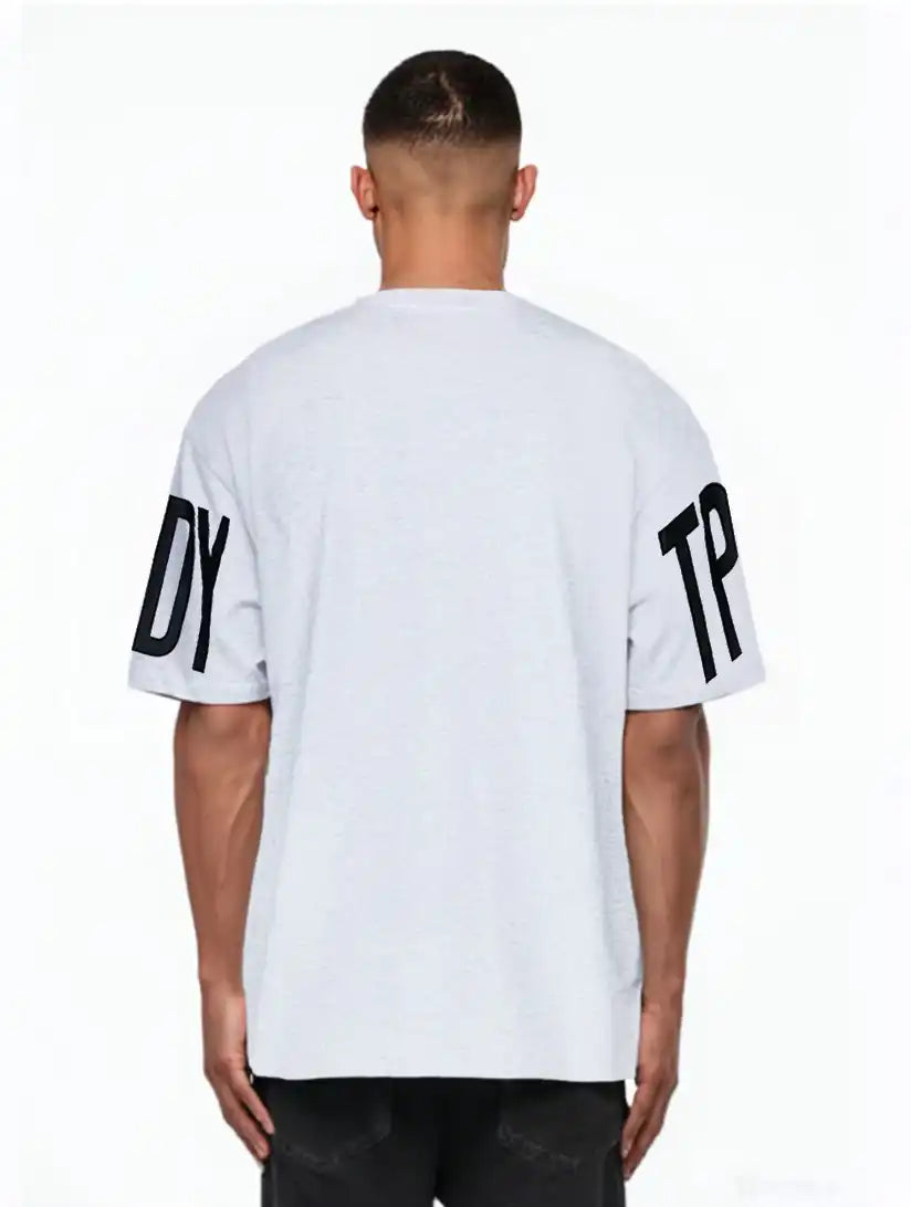 Eine Person schaut von der Kamera weg und trägt das trueprodigy Viktor Oversize-Herren-T-Shirt mit Front- und Ärmelprints in Hellgrau mit auffälligen schwarzen DY- und TP-Ärmelprints, gepaart mit einer dunklen Hose.