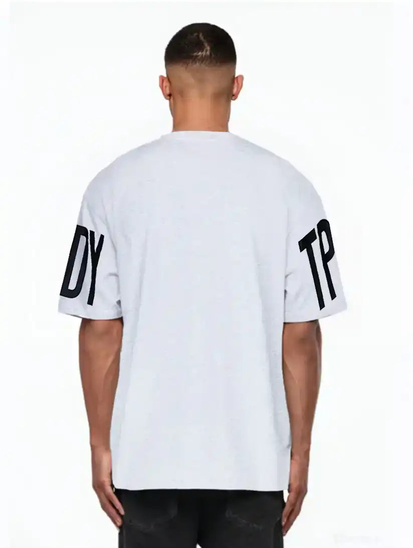 Eine Person schaut von der Kamera weg und trägt das trueprodigy Viktor Oversize-Herren-T-Shirt mit Front- und Ärmelprints in Hellgrau mit auffälligen schwarzen DY- und TP-Ärmelprints, gepaart mit einer dunklen Hose.