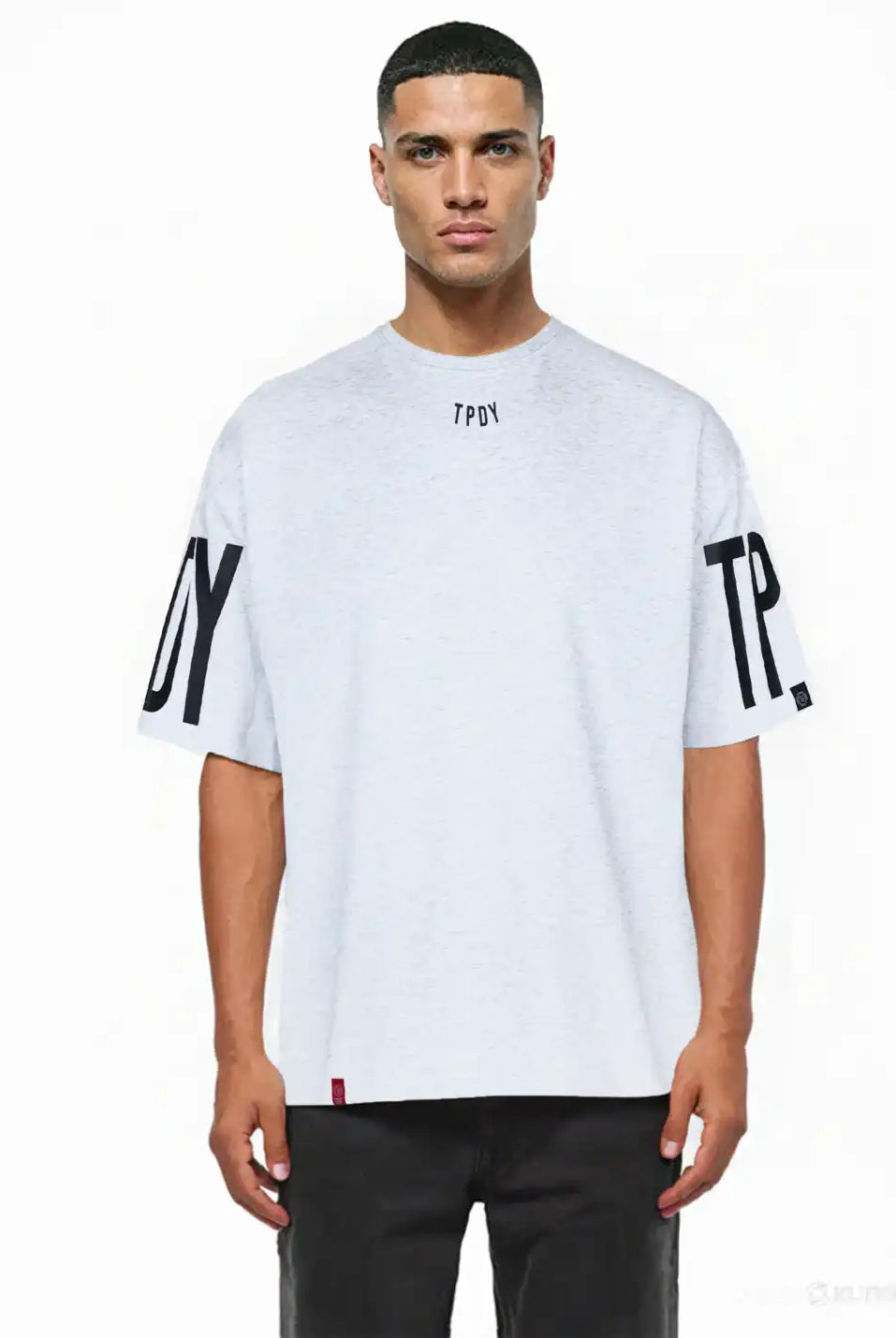 Ein Mann mit kurzen Haaren modelliert das Viktor Oversize-Herren-T-Shirt von trueprodigy. Dieses lockere, schwere Jersey-Shirt in Hellgrau hat schwarze TPDY-Prints auf dem Kragen und den Ärmeln. Er posiert vor einem schlichten weißen Hintergrund.