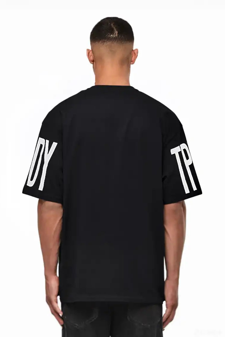 Ein Mann blickt von der Kamera weg und trägt das trueprodigy Viktor Oversize-Herren-T-Shirt mit schwerem Jersey-Stoff und großen weißen "TPD"- und "Y"-Ärmelaufdrucken vor einem schlichten weißen Hintergrund.