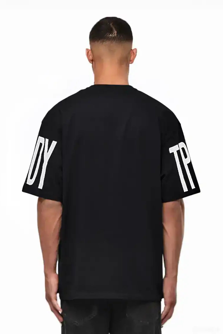 Ein Mann blickt von der Kamera weg und trägt das trueprodigy Viktor Oversize-Herren-T-Shirt mit schwerem Jersey-Stoff und großen weißen "TPD"- und "Y"-Ärmelaufdrucken vor einem schlichten weißen Hintergrund.