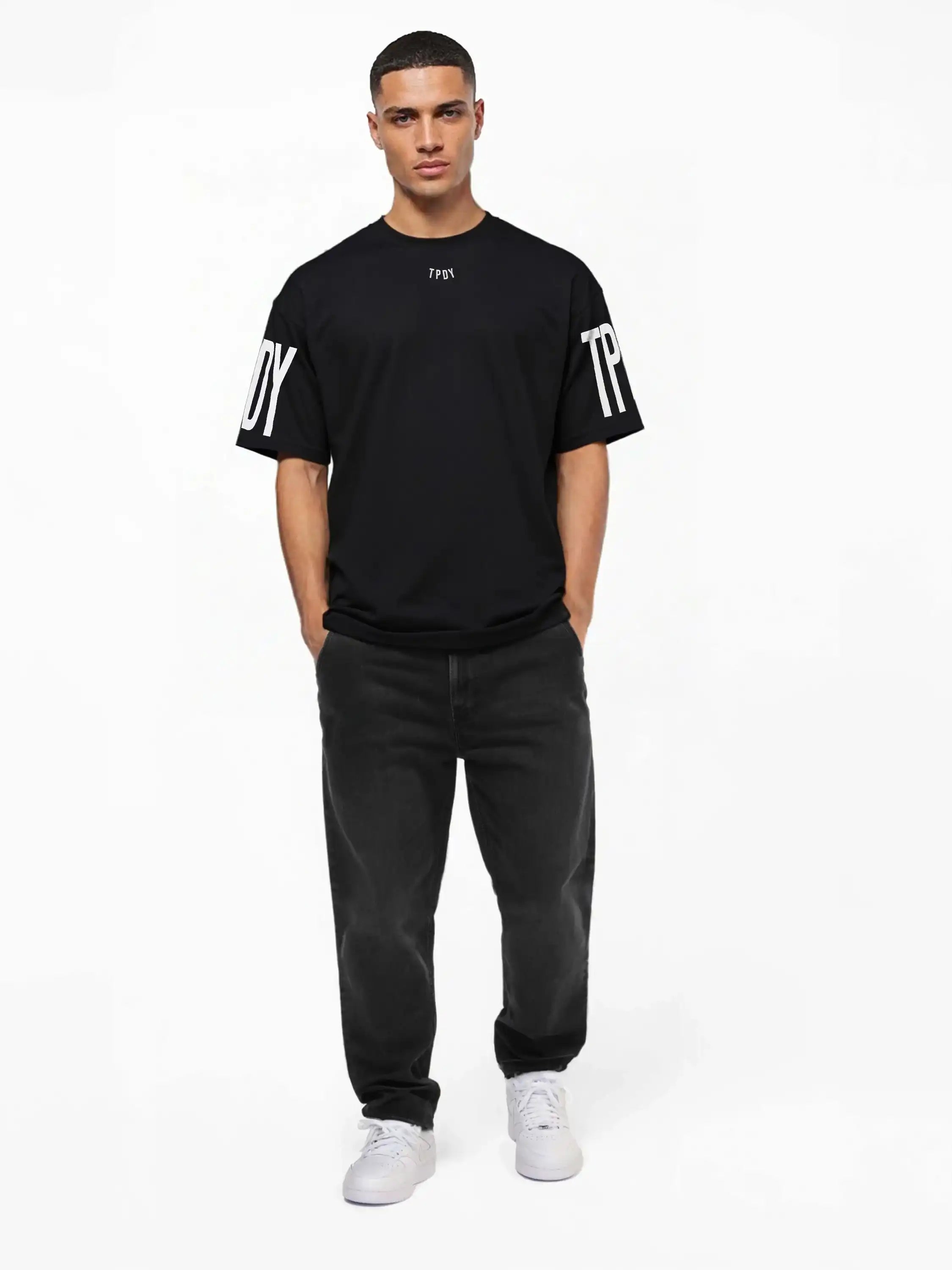 Ein Mann blickt mit den Händen in den Taschen nach vorne und trägt das trueprodigy Viktor Oversize-Herren-T-Shirt mit Front- und Ärmelprints, gepaart mit dunklen Jeans und weißen Turnschuhen vor einem schlichten weißen Hintergrund.