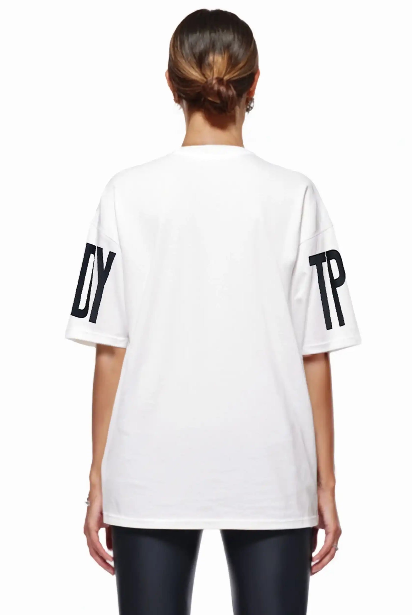 Eine Person mit braunen Haaren in einem tiefen Dutt ist von hinten zu sehen. Sie trägt das trueprodigy Viktor F Oversize-Damen-T-Shirt mit Ärmelprints und Frontprint unter dem Kragen, gestylt mit einer schwarzen Hose.