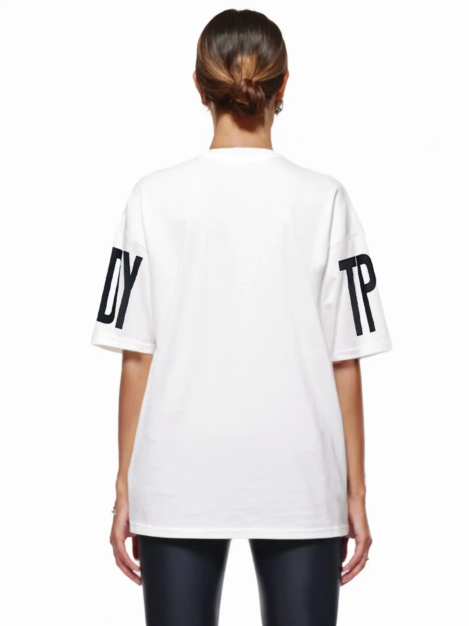 Eine Person mit braunen Haaren in einem tiefen Dutt ist von hinten zu sehen. Sie trägt das trueprodigy Viktor F Oversize-Damen-T-Shirt mit Ärmelprints und Frontprint unter dem Kragen, gestylt mit einer schwarzen Hose.