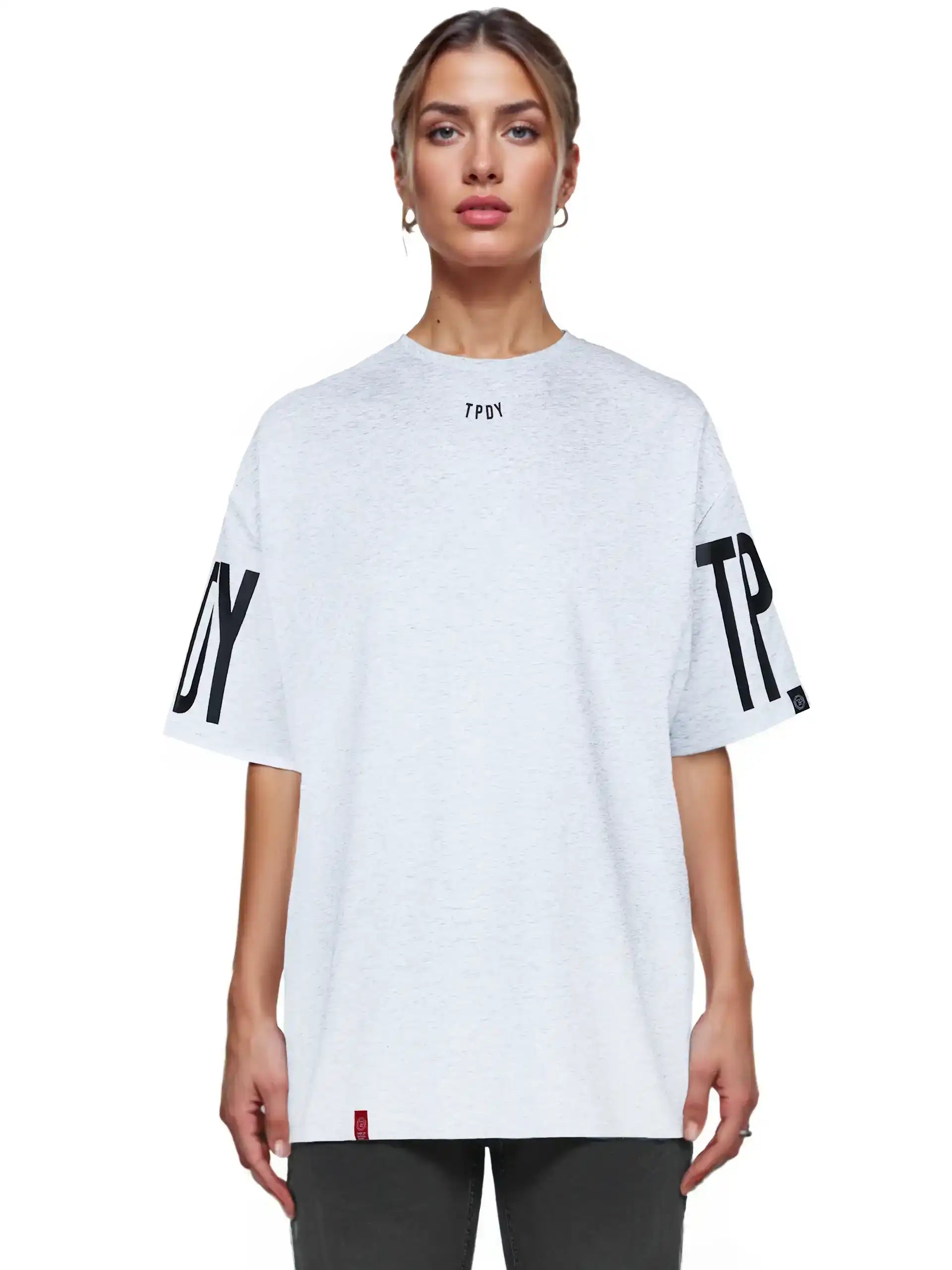 Eine Person mit zurückgebundenem Haar trägt das Viktor F Oversize-Damen-T-Shirt mit Ärmelprints und Frontprint unter dem Kragen von trueprodigy in Hellgrau, gepaart mit einer dunklen Hose, und steht mit dem Gesicht nach vorne vor einem schlichten weißen Hintergrund.