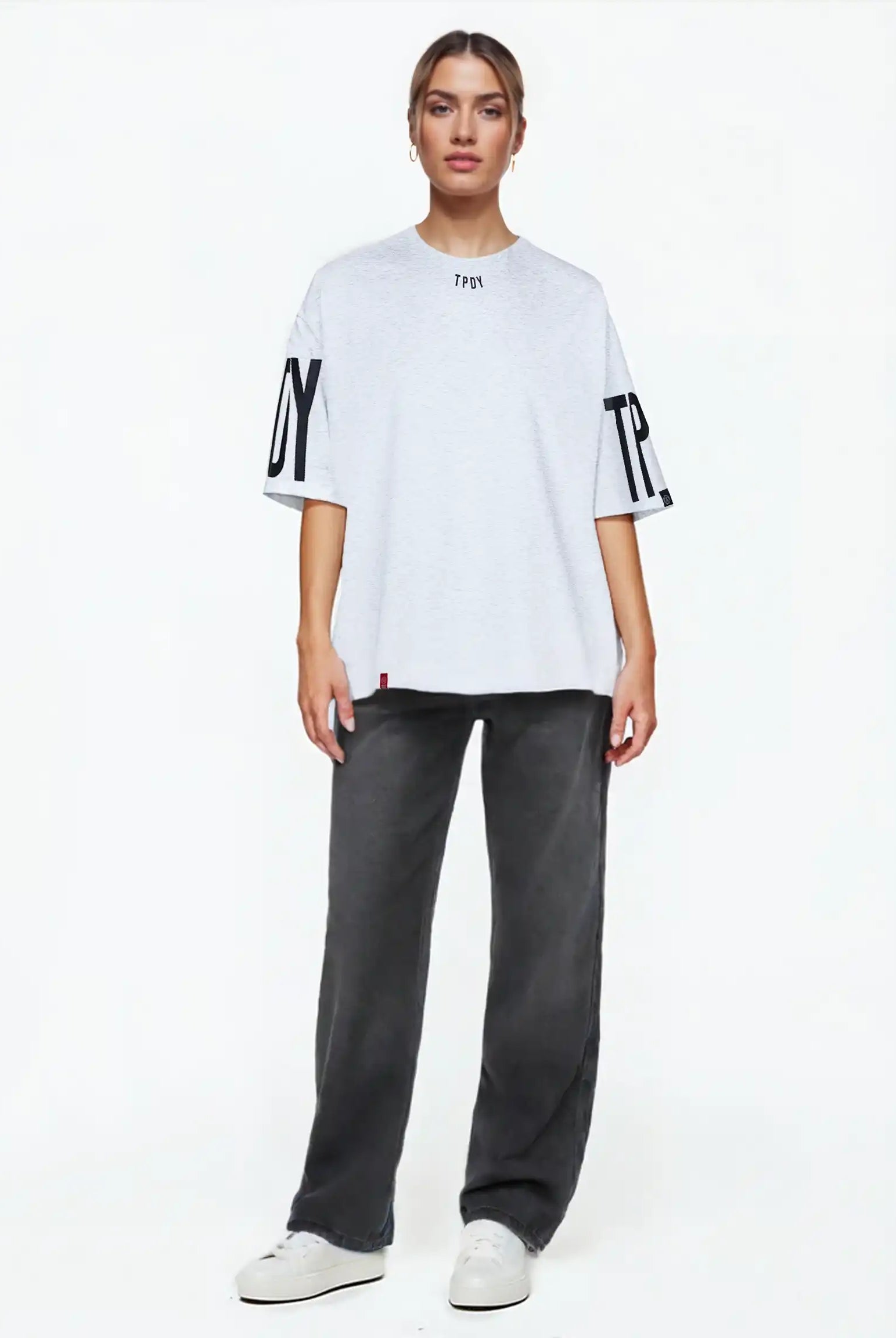 Eine Person steht mit dem Viktor F Oversize-Damen-T-Shirt mit Ärmelprints und Frontprint unter dem Kragen von trueprodigy, gestylt mit dunkelgrauen Jeans und weißen Turnschuhen, vor einem schlichten weißen Hintergrund.