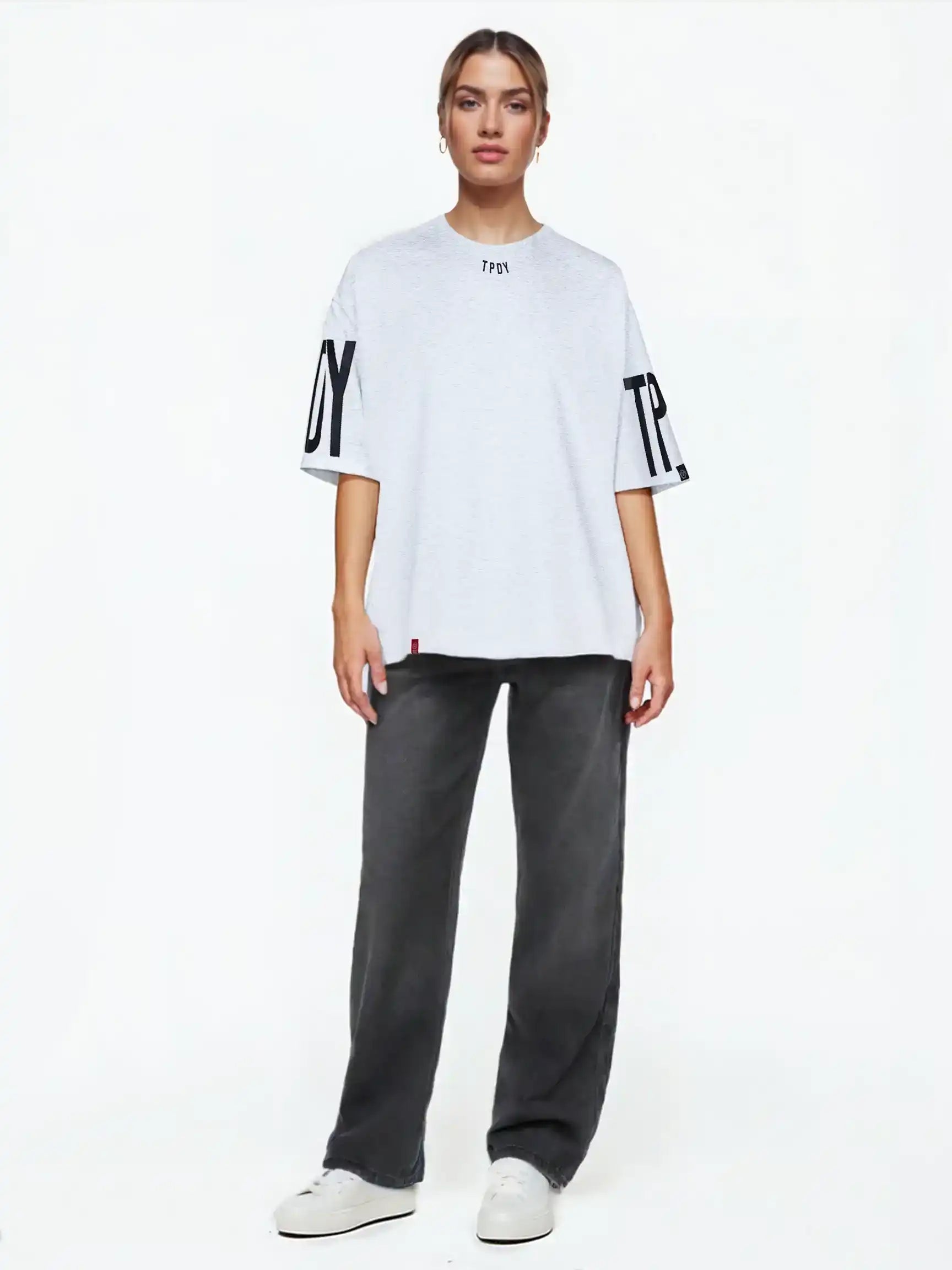 Eine Person steht mit dem Viktor F Oversize-Damen-T-Shirt mit Ärmelprints und Frontprint unter dem Kragen von trueprodigy, gestylt mit dunkelgrauen Jeans und weißen Turnschuhen, vor einem schlichten weißen Hintergrund.