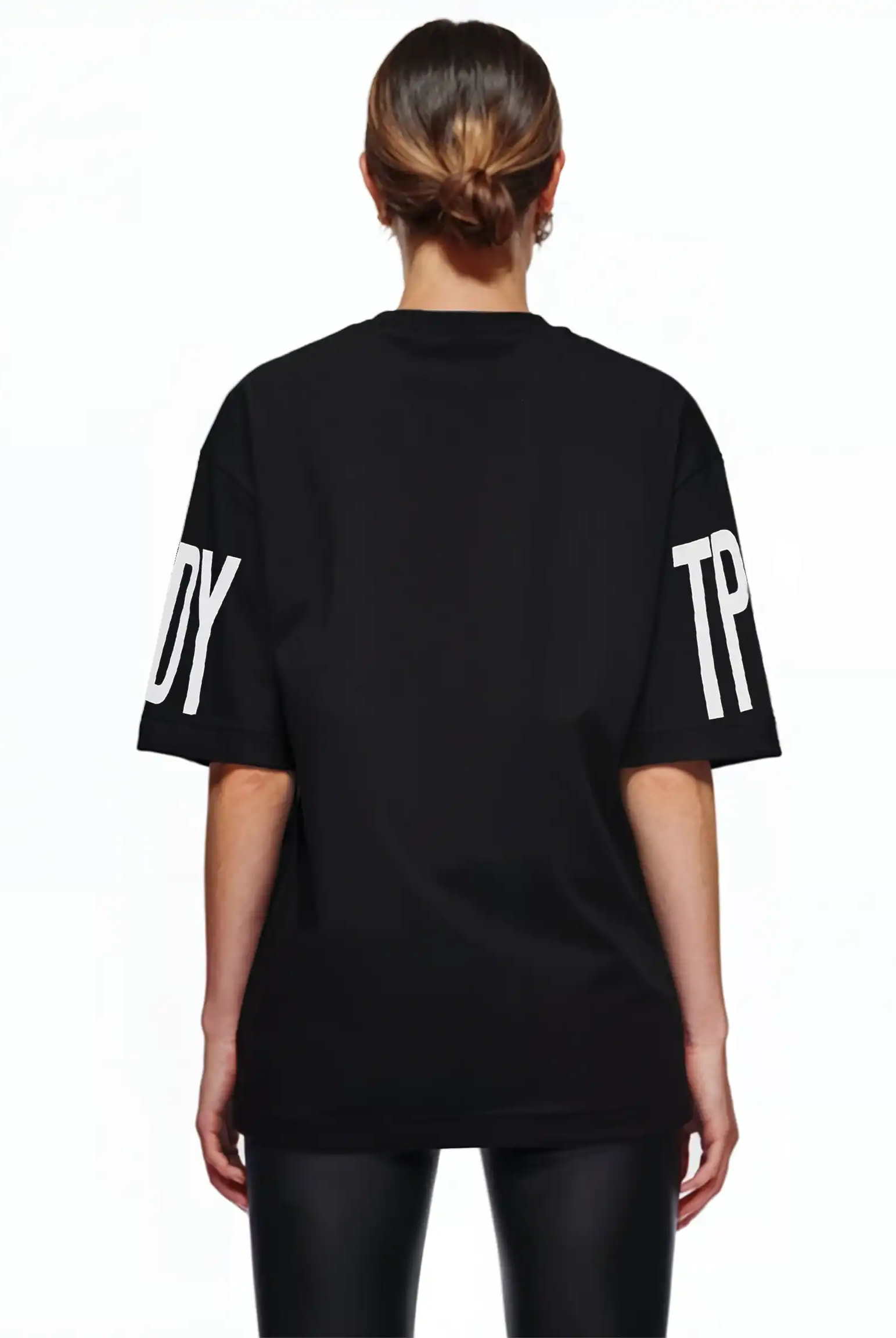 Man sieht eine Person mit braunen Haaren in einem tiefen Dutt von hinten, die das trueprodigy Viktor F Oversize-Damen-T-Shirt mit Ärmelprints und Frontprint unter dem Kragen und eine schwarz glänzende Hose trägt und vor einem weißen Hintergrund steht.