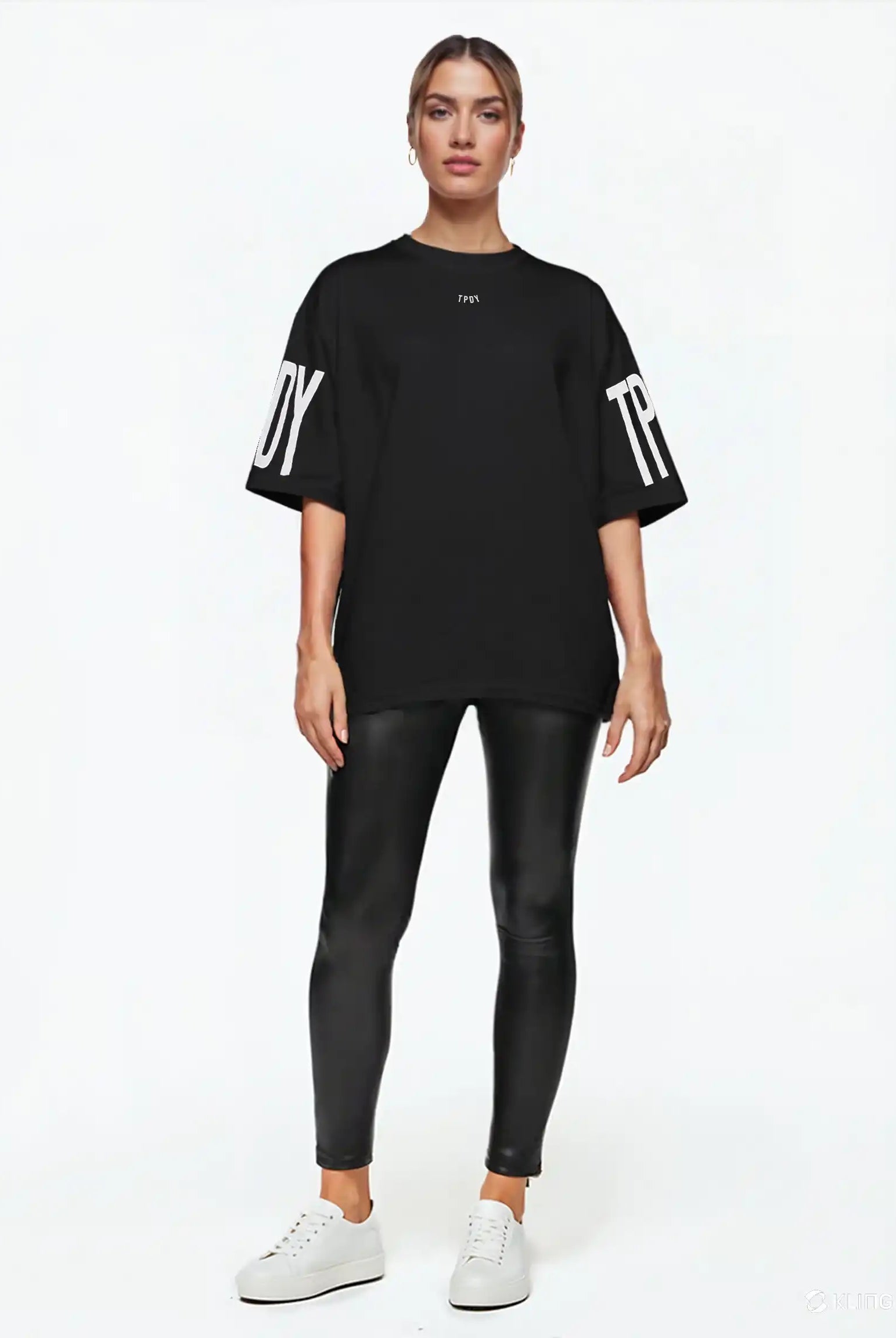 Eine Person blickt nach vorne und trägt das trueprodigy Viktor F Oversize-Damen-T-Shirt mit Ärmelprints und Frontprint unter dem Kragen, gepaart mit schwarzen Leggings in Lederoptik und weißen Sneakers, vor einem schlichten weißen Hintergrund.