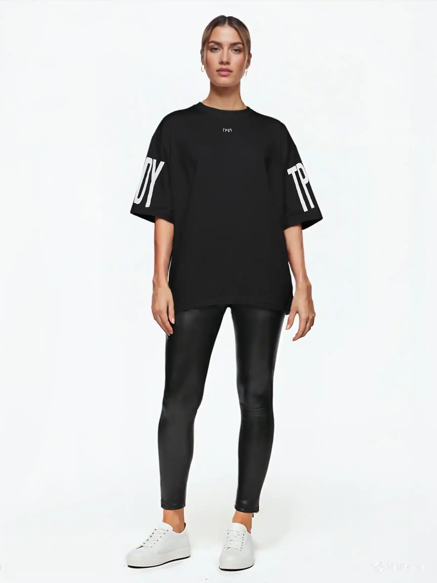 Eine Person blickt nach vorne und trägt das trueprodigy Viktor F Oversize-Damen-T-Shirt mit Ärmelprints und Frontprint unter dem Kragen, gepaart mit schwarzen Leggings in Lederoptik und weißen Sneakers, vor einem schlichten weißen Hintergrund.