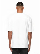 Ein Mann schaut von der Kamera weg und trägt das trueprodigy Nika Oversize-Basicshirt mit TPDY-Stickerei & klarer Silhouette in weiß und dunkler Hose. Der Hintergrund ist einfarbig weiß.