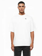 Ein Mann steht mit dem trueprodigy Nika Oversize-Basicshirt mit TPDY-Stickerei & klarer Silhouette, gepaart mit einer schwarzen Hose, vor einem weißen Hintergrund.