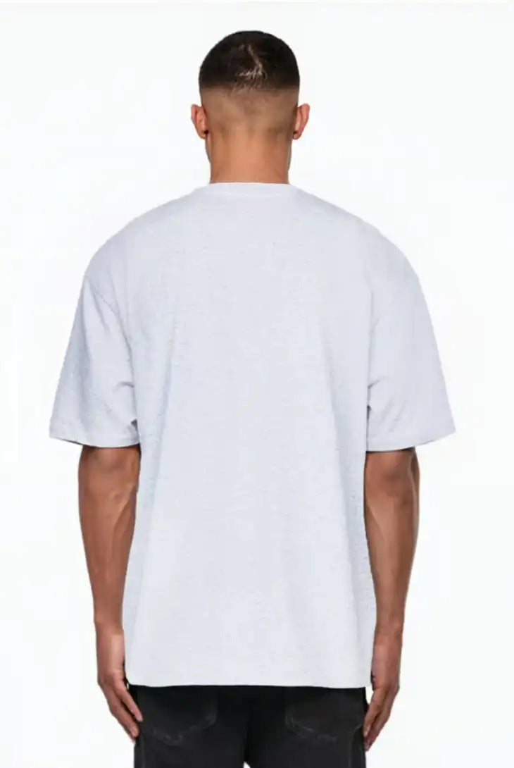 Ein Mann, der mit dem Rücken zur Kamera steht, trägt das trueprodigy Nika Oversize-Basicshirt mit TPDY-Stickerei & klarer Silhouette in hellgrau und schwarzer Hose, posiert vor einem weißen Hintergrund.