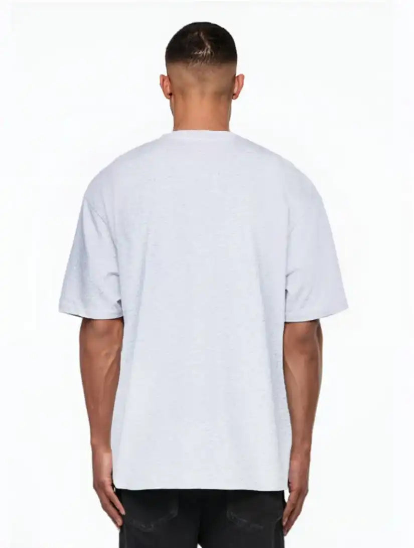 Ein Mann, der mit dem Rücken zur Kamera steht, trägt das trueprodigy Nika Oversize-Basicshirt mit TPDY-Stickerei & klarer Silhouette in hellgrau und schwarzer Hose, posiert vor einem weißen Hintergrund.