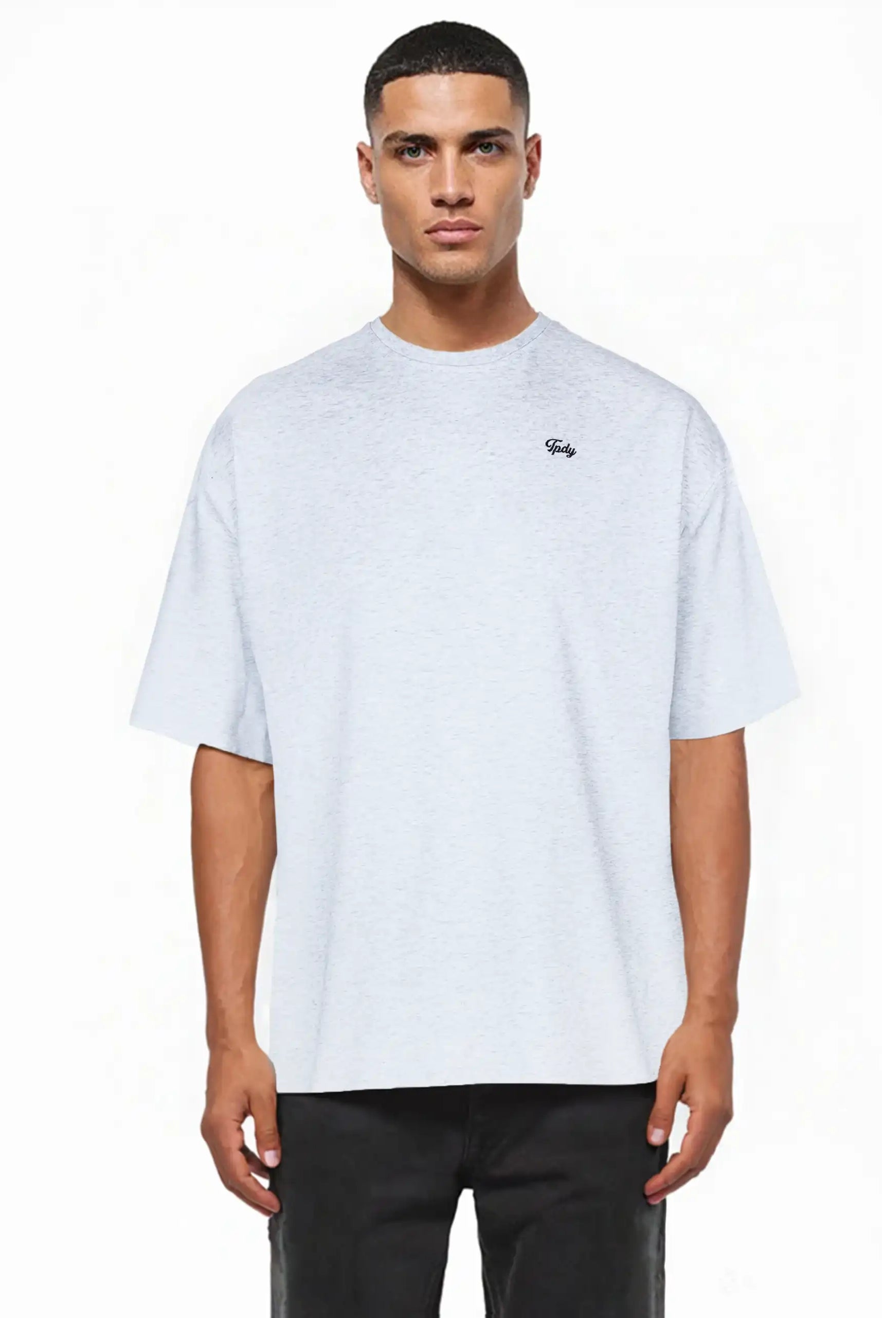 Ein Mann sieht nach vorne und trägt ein lockeres, hellgraues Nika Oversize-Basicshirt mit TPDY-Stickerei & klarer Silhouette von trueprodigy mit kurzen Ärmeln und einem kleinen Logo auf der linken Brust, gepaart mit einer schwarzen Hose. Der Hintergrund ist einfarbig weiß.