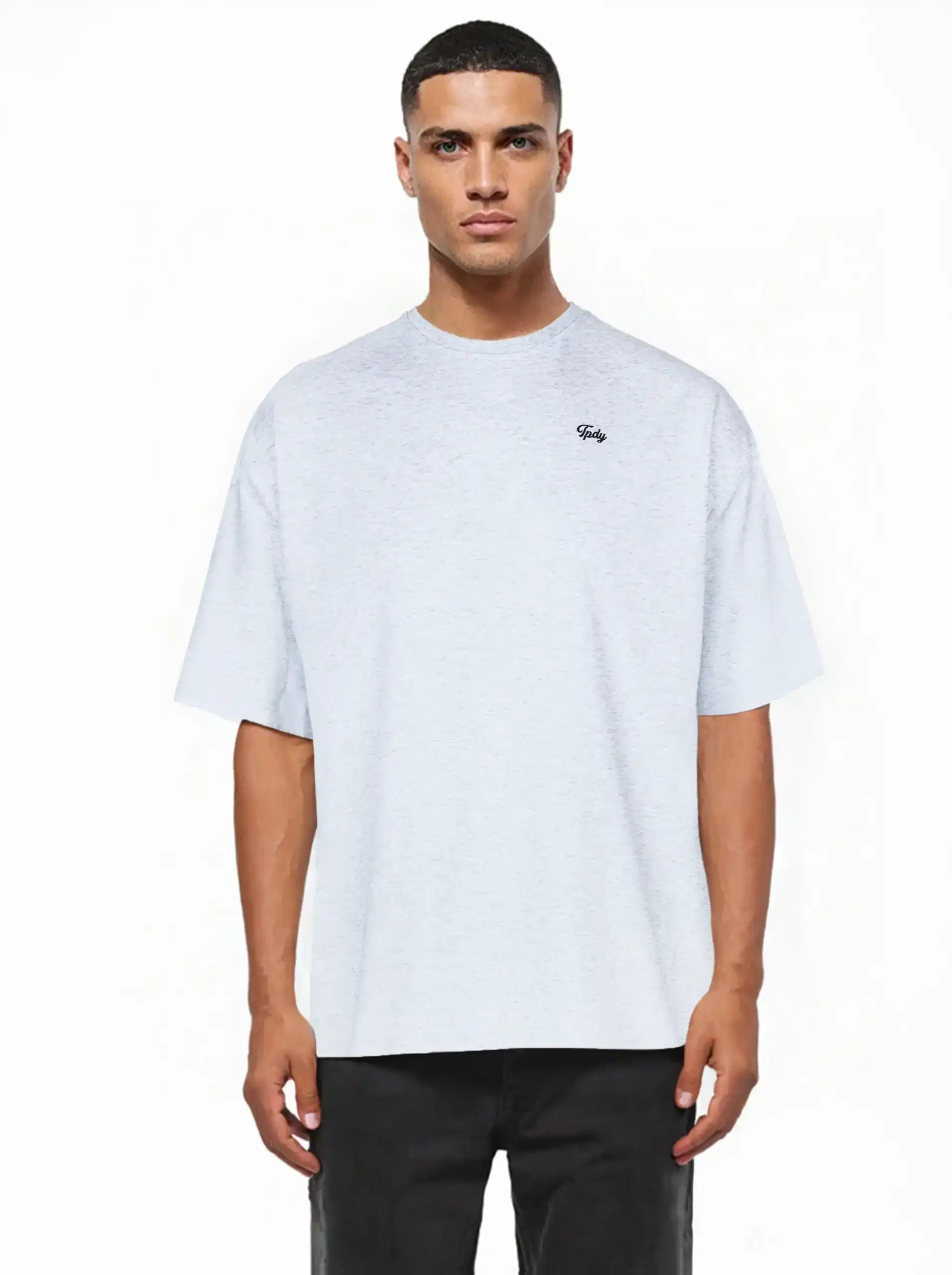Ein Mann sieht nach vorne und trägt ein lockeres, hellgraues Nika Oversize-Basicshirt mit TPDY-Stickerei & klarer Silhouette von trueprodigy mit kurzen Ärmeln und einem kleinen Logo auf der linken Brust, gepaart mit einer schwarzen Hose. Der Hintergrund ist einfarbig weiß.