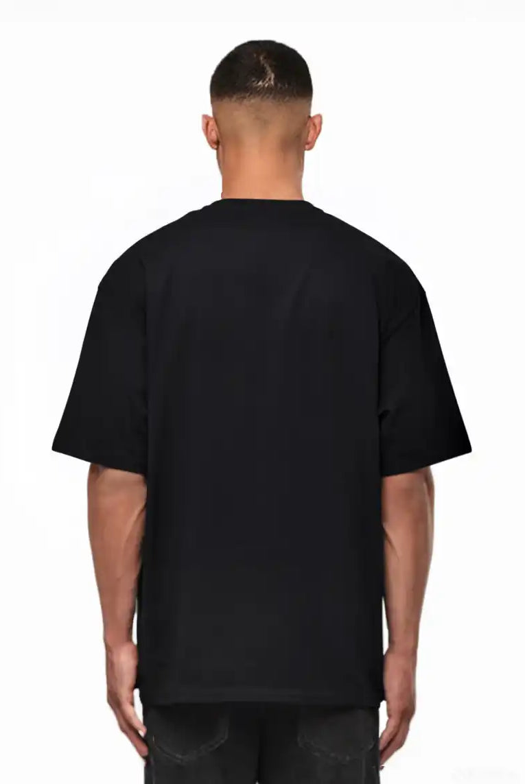 Ein Mann schaut von der Kamera weg, trägt ein schwarzes trueprodigy Noa Oversize-Shirt mit "FEAR NOTHING"-Print & handschriftlichem Detail und dunkle Jeans, vor einem weißen Hintergrund.