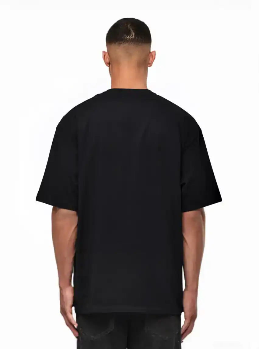 Ein Mann schaut von der Kamera weg, trägt ein schwarzes trueprodigy Noa Oversize-Shirt mit "FEAR NOTHING"-Print & handschriftlichem Detail und dunkle Jeans, vor einem weißen Hintergrund.