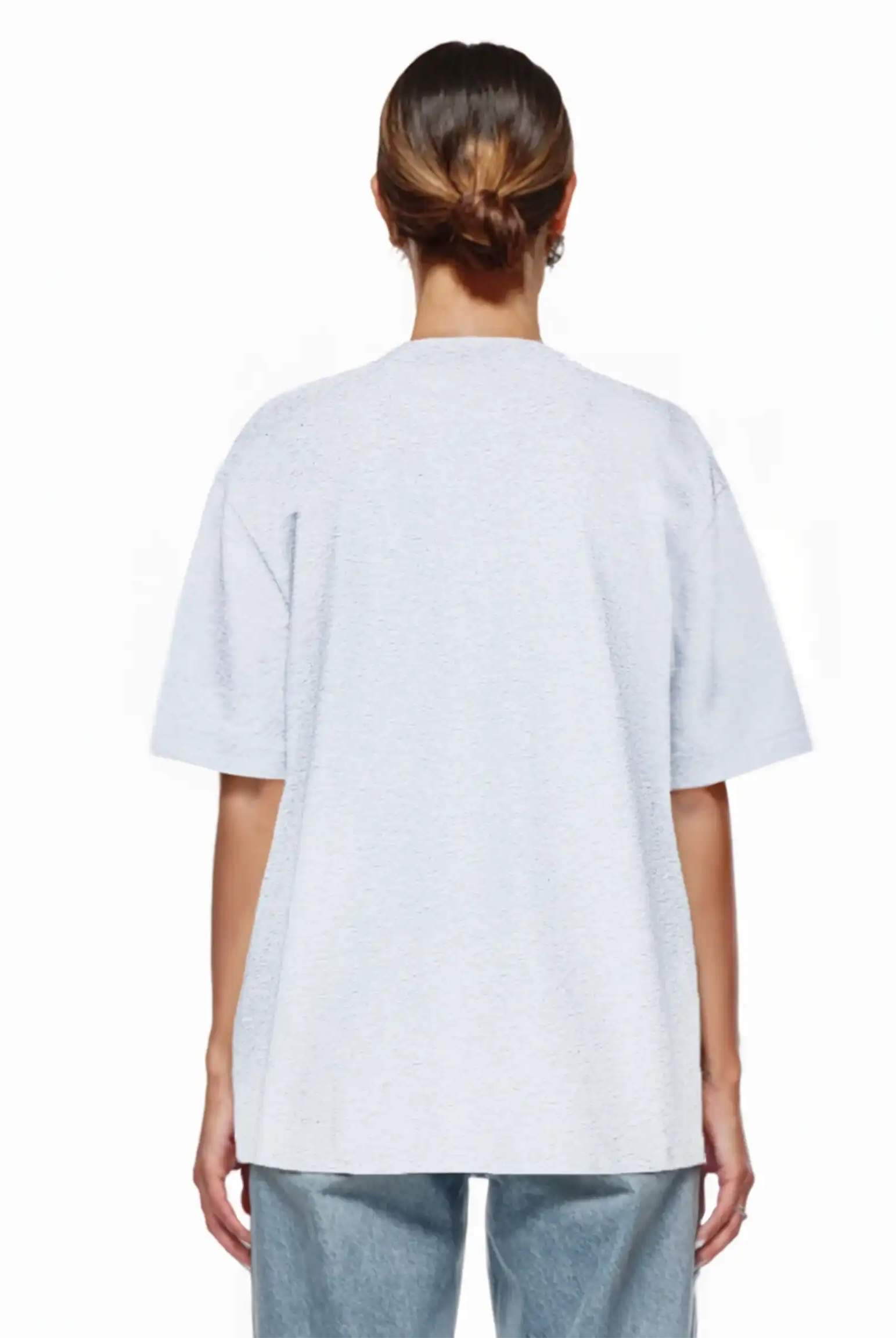 Eine Person mit braunen Haaren in einem tiefen Dutt ist von hinten zu sehen. Sie trägt das trueprodigy Nika F Damen Oversize-T-Shirt mit TPDY-Stickerei auf der Brust und hellblaue Jeans, vor einem schlichten weißen Hintergrund.