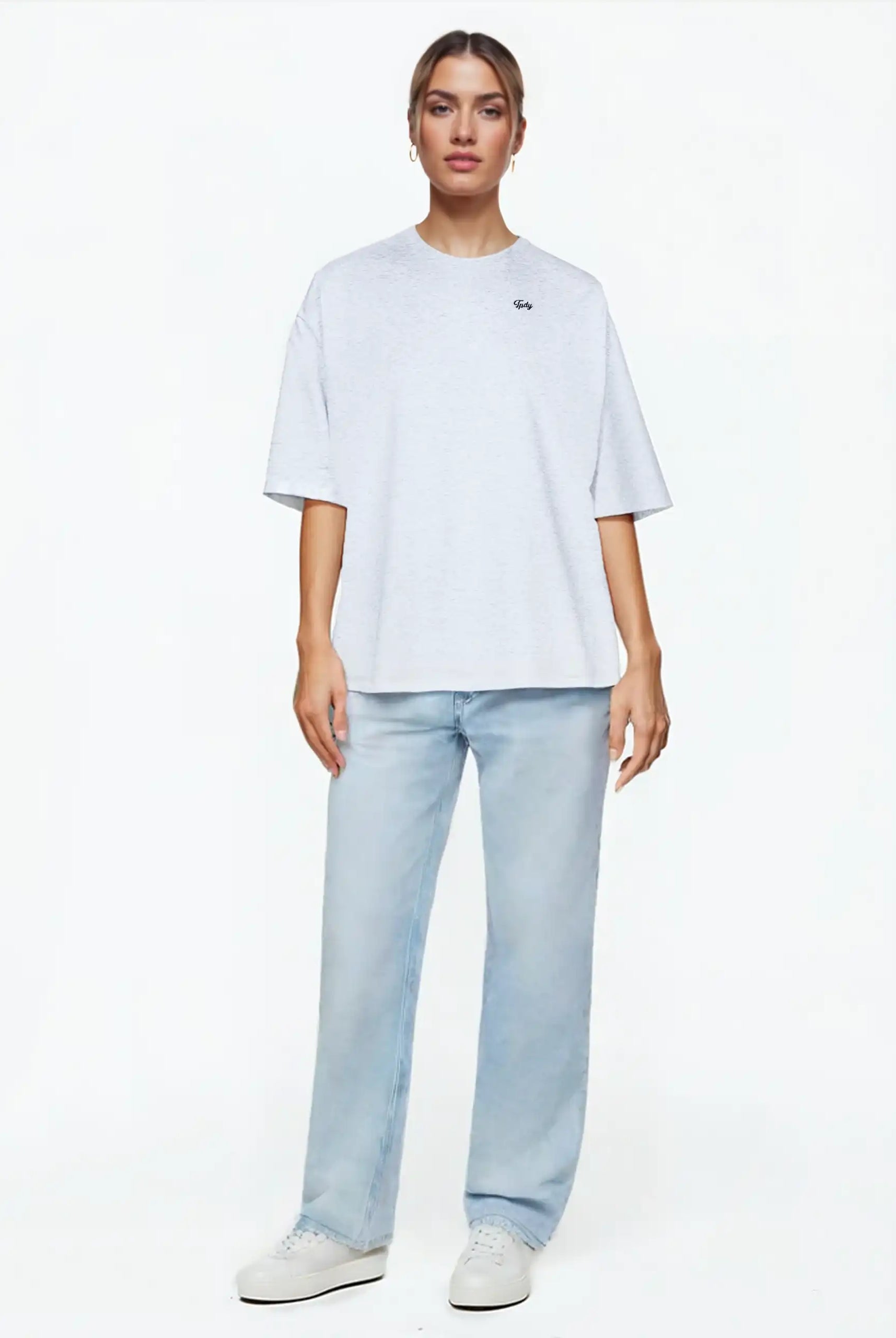 Eine Person steht mit Blick nach vorne und trägt das Nika F Damen Oversize-T-Shirt mit TPDY-Stickerei auf der Brust von trueprodigy in Hellgrau, gepaart mit hellblauen Jeans und weißen Turnschuhen vor einem schlichten weißen Hintergrund.