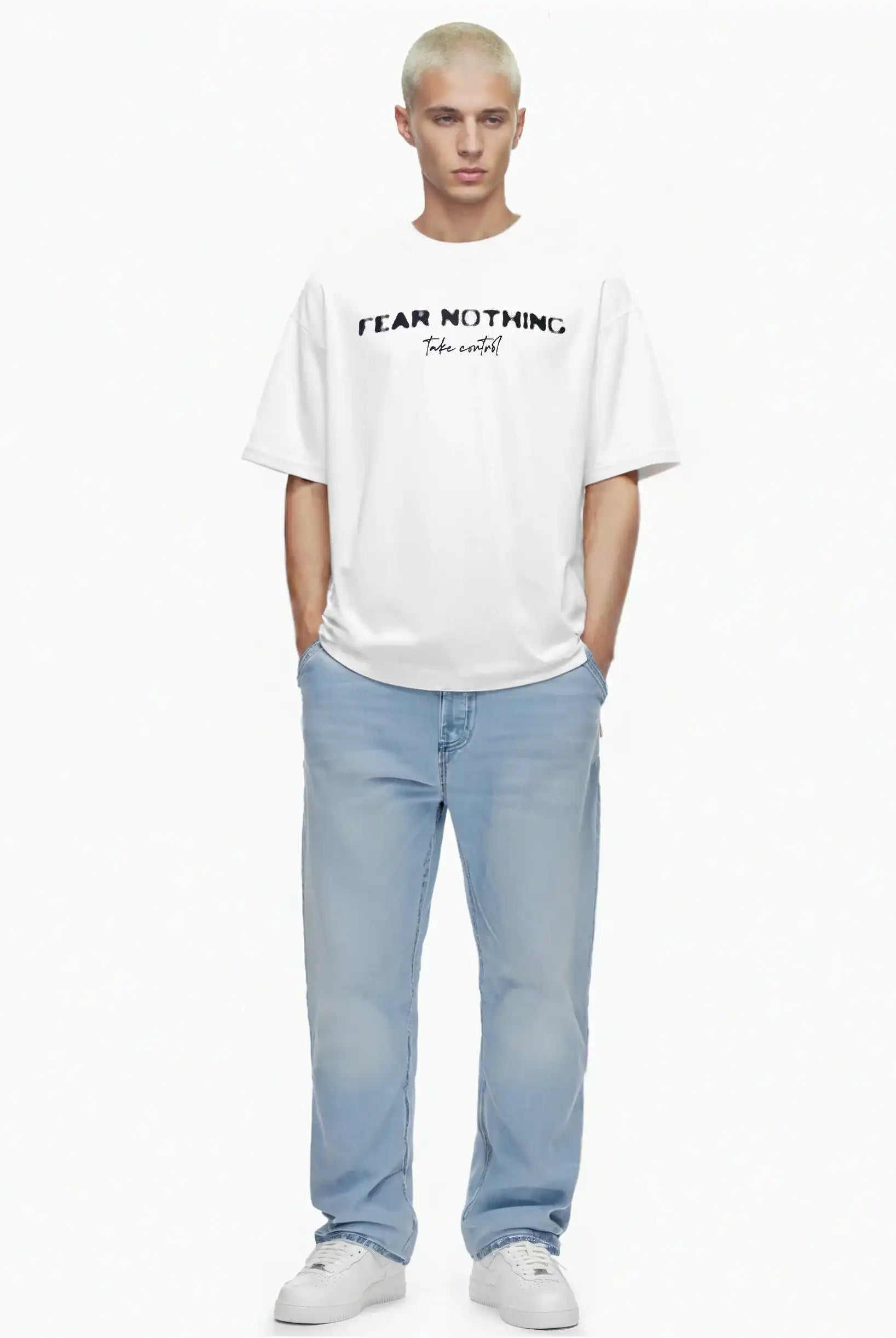 Eine Person mit kurzen blonden Haaren steht vor einem weißen Hintergrund, trägt das trueprodigy Noa Oversize-Shirt mit "FEAR NOTHING"-Print & handschriftlichem Detail, hellblaue Jeans und weiße Turnschuhe. Die Hände stecken in den Taschen.
