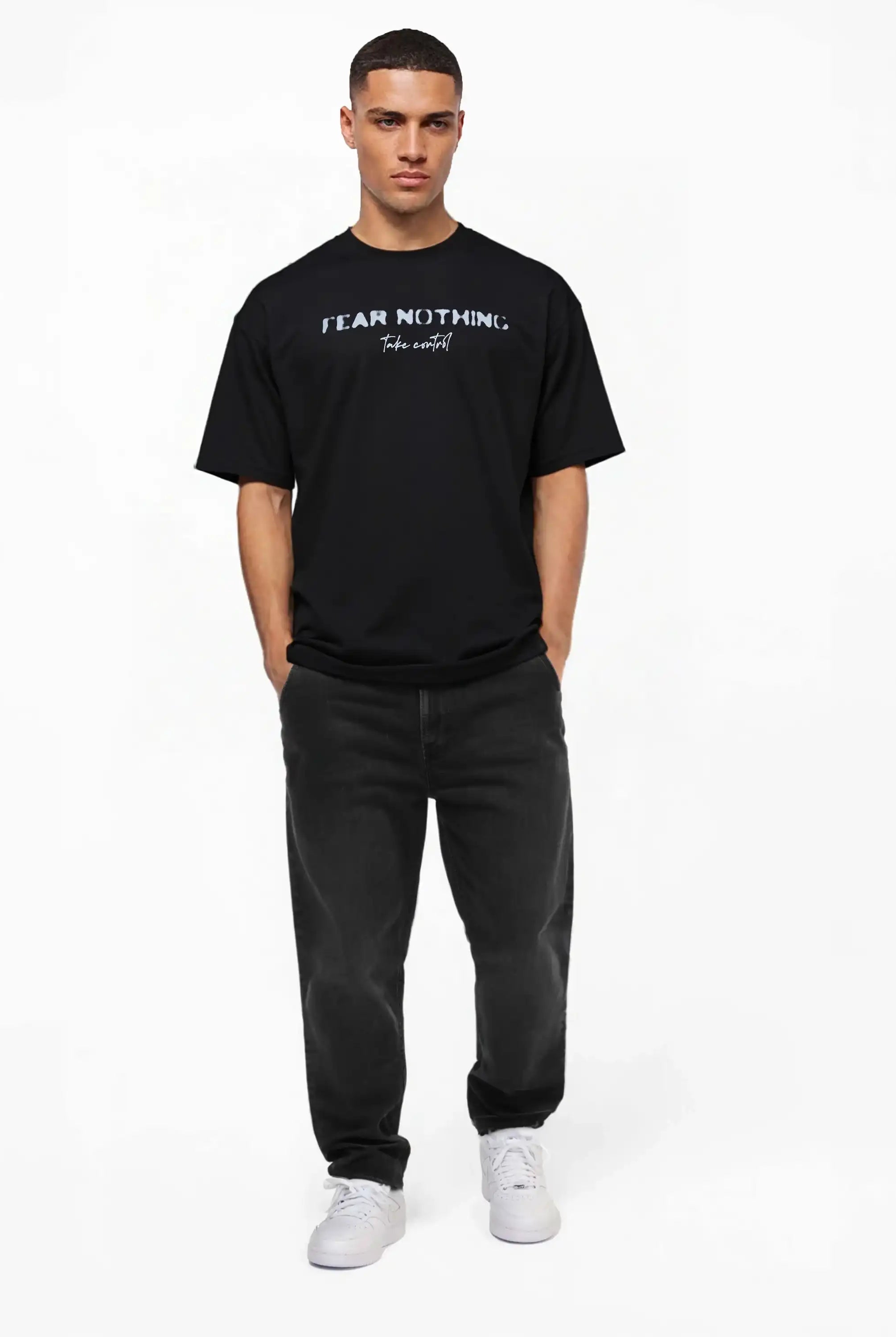 Ein Mann steht vor einem schlichten weißen Hintergrund und trägt das trueprodigy Noa Oversize-Shirt mit dem Aufdruck "FEAR NOTHING" und handschriftlichen Details, schwarze Jeans und weiße Turnschuhe. Seine Hände stecken in den Taschen, während er geradeaus schaut.