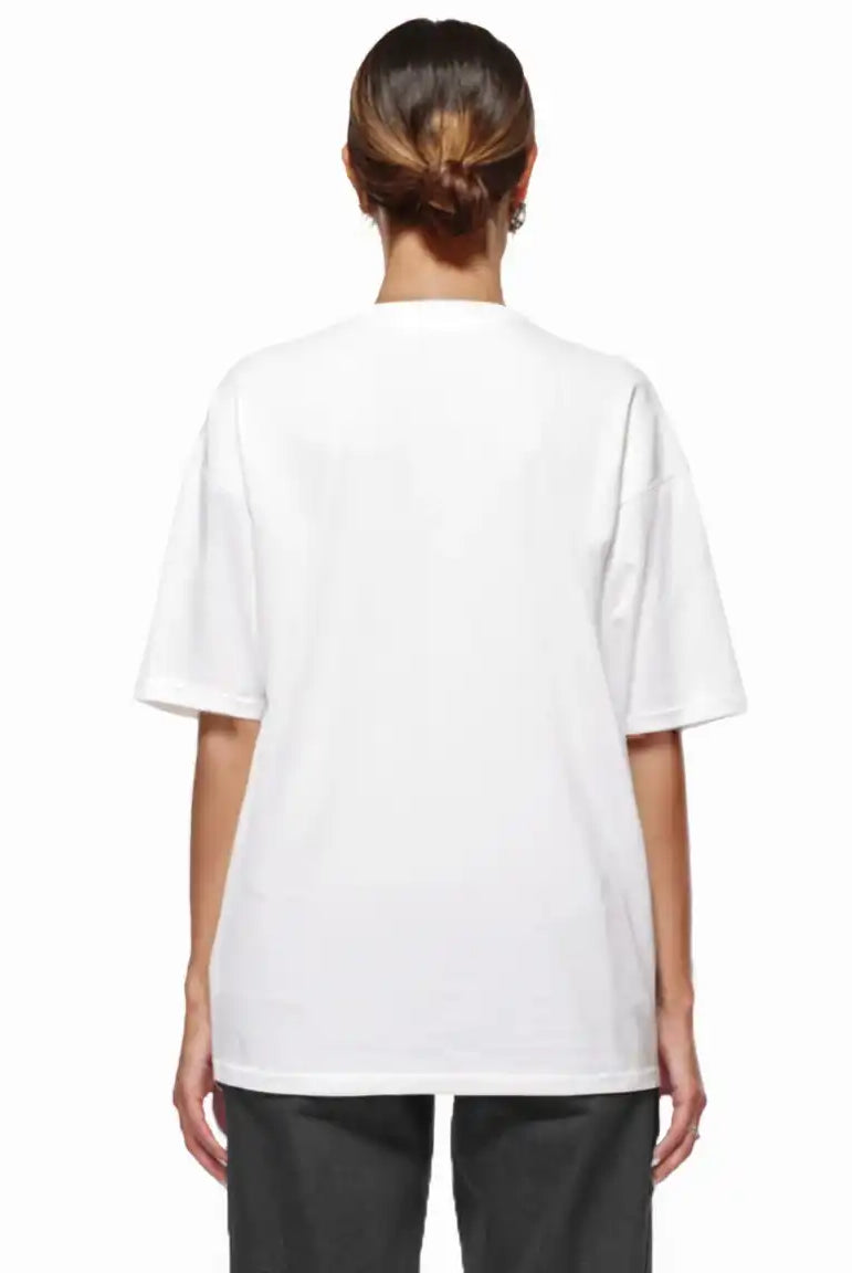 Eine Person steht mit dem Rücken zur Kamera, trägt das trueprodigy Noa F Oversize-T-Shirt mit "FEAR NOTHING" & "take control"-Frontprint in schwerem Jerseystoff und dunkler Hose, die Haare nach hinten gebunden, vor einem weißen Hintergrund.