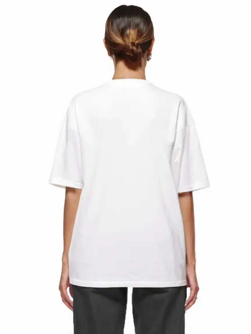 Eine Person steht mit dem Rücken zur Kamera, trägt das trueprodigy Noa F Oversize-T-Shirt mit "FEAR NOTHING" & "take control"-Frontprint in schwerem Jerseystoff und dunkler Hose, die Haare nach hinten gebunden, vor einem weißen Hintergrund.