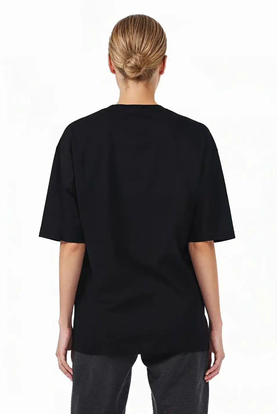 Eine Person mit blonden Haaren in einem tiefen Dutt, die von der Kamera wegschaut, trägt das trueprodigy Noa F Oversize-T-Shirt mit "FEAR NOTHING" & "take control"-Frontprint aus schwerem Jerseystoff und eine dunkle Hose vor einem schlichten weißen Hintergrund.