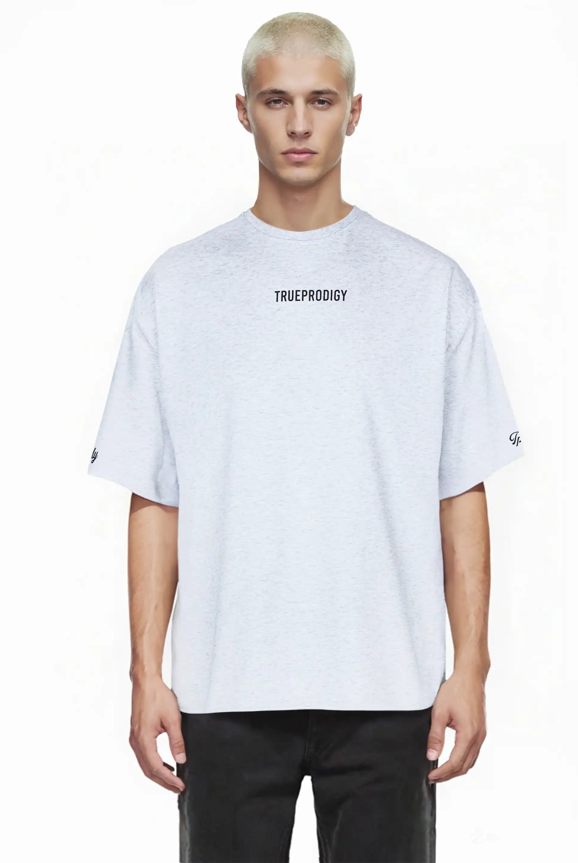 Ein junger Mann mit kurzen, gebleichten blonden Haaren blickt nach vorne in einem hellgrauen Kai Oversize-Herren-T-Shirt von trueprodigy mit Markenlogo vorne, Rückenprint "LIMITLESS" und schwarzen Hosen.